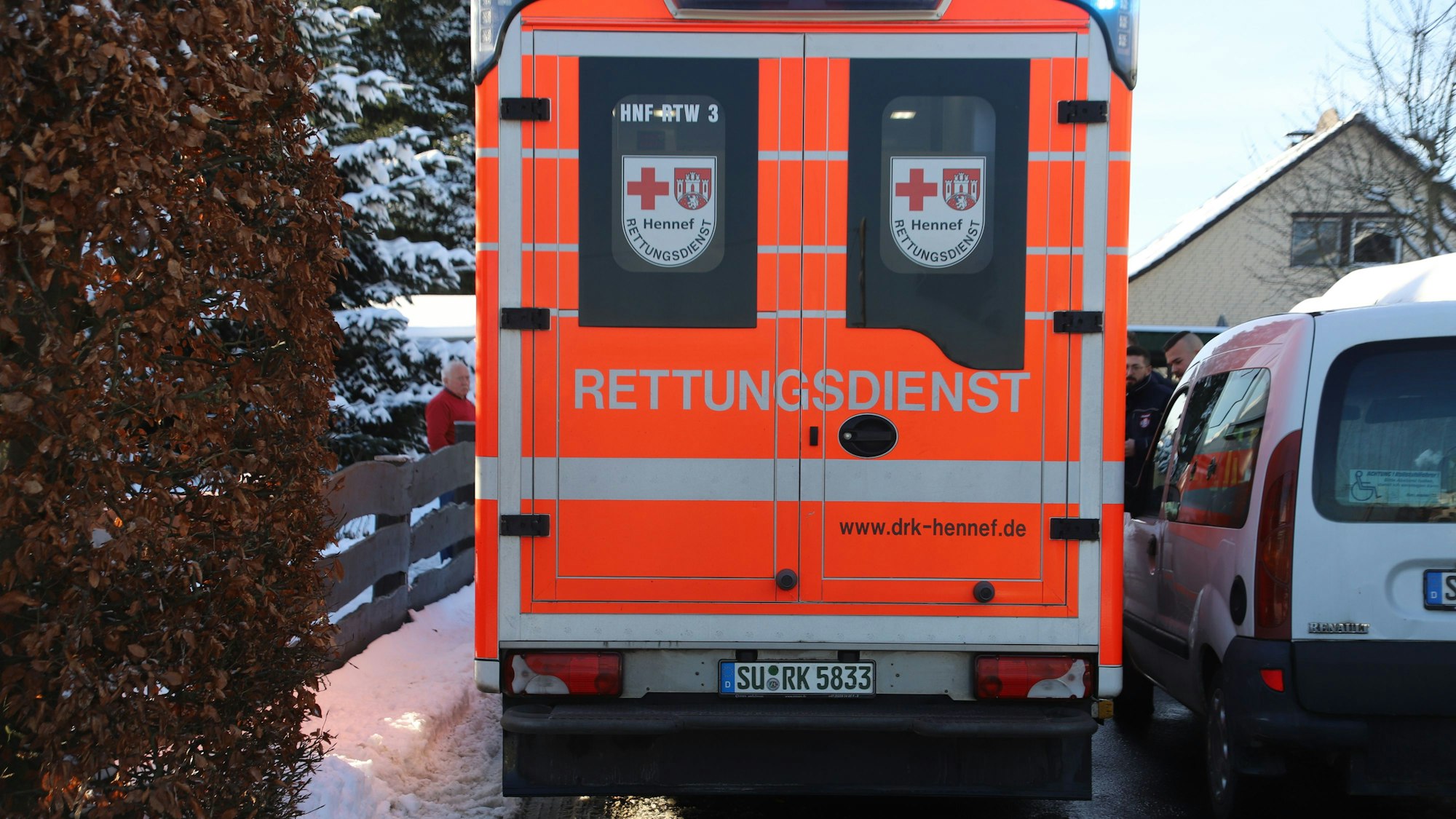 Ein Rettungsfahrzeug fährt durch eine schneebedeckte Straße nur Zentimeter an einem geparkten Fahrzeug vorbei.
