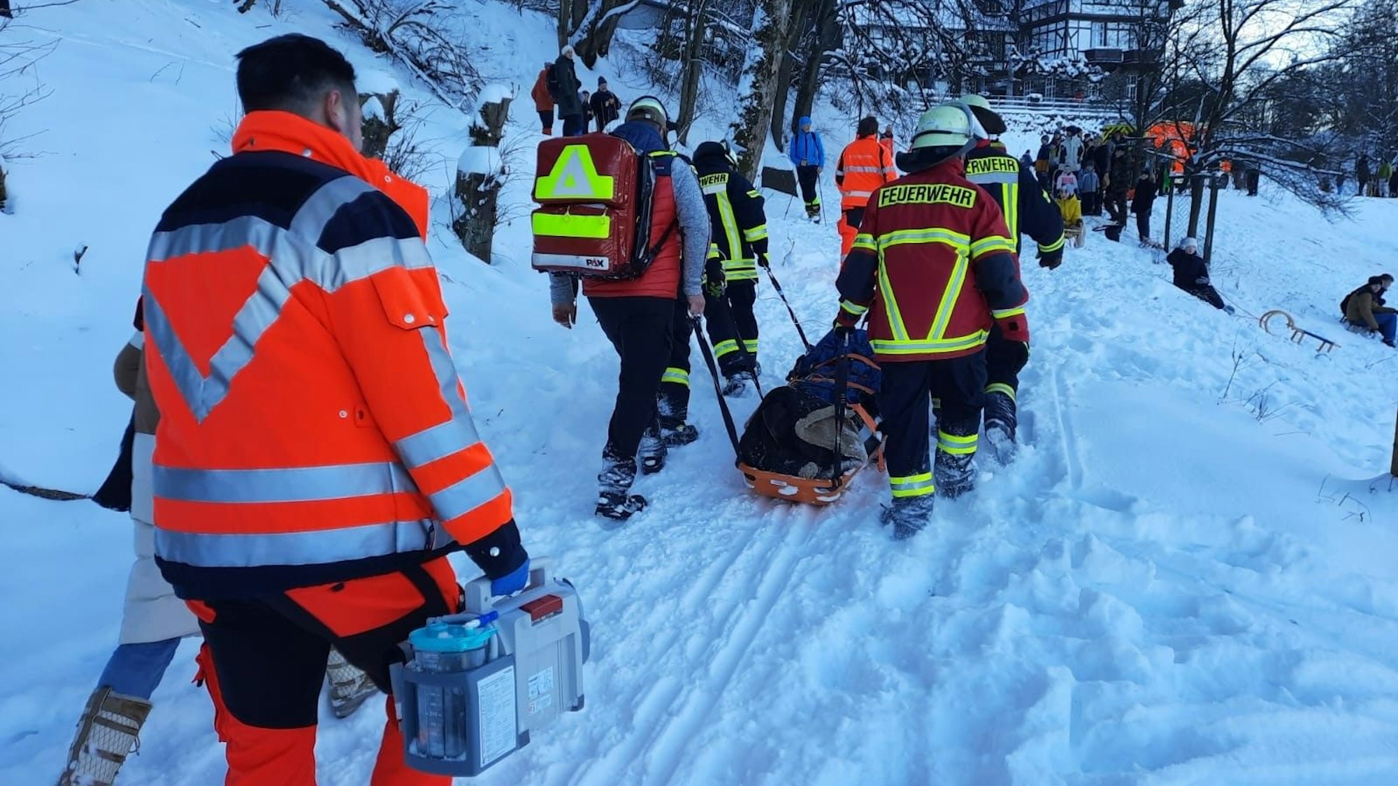 Rettungskäfte ziehen eine Schleifkorbtrage durch den tiefen Schnee einen Weg hinauf.