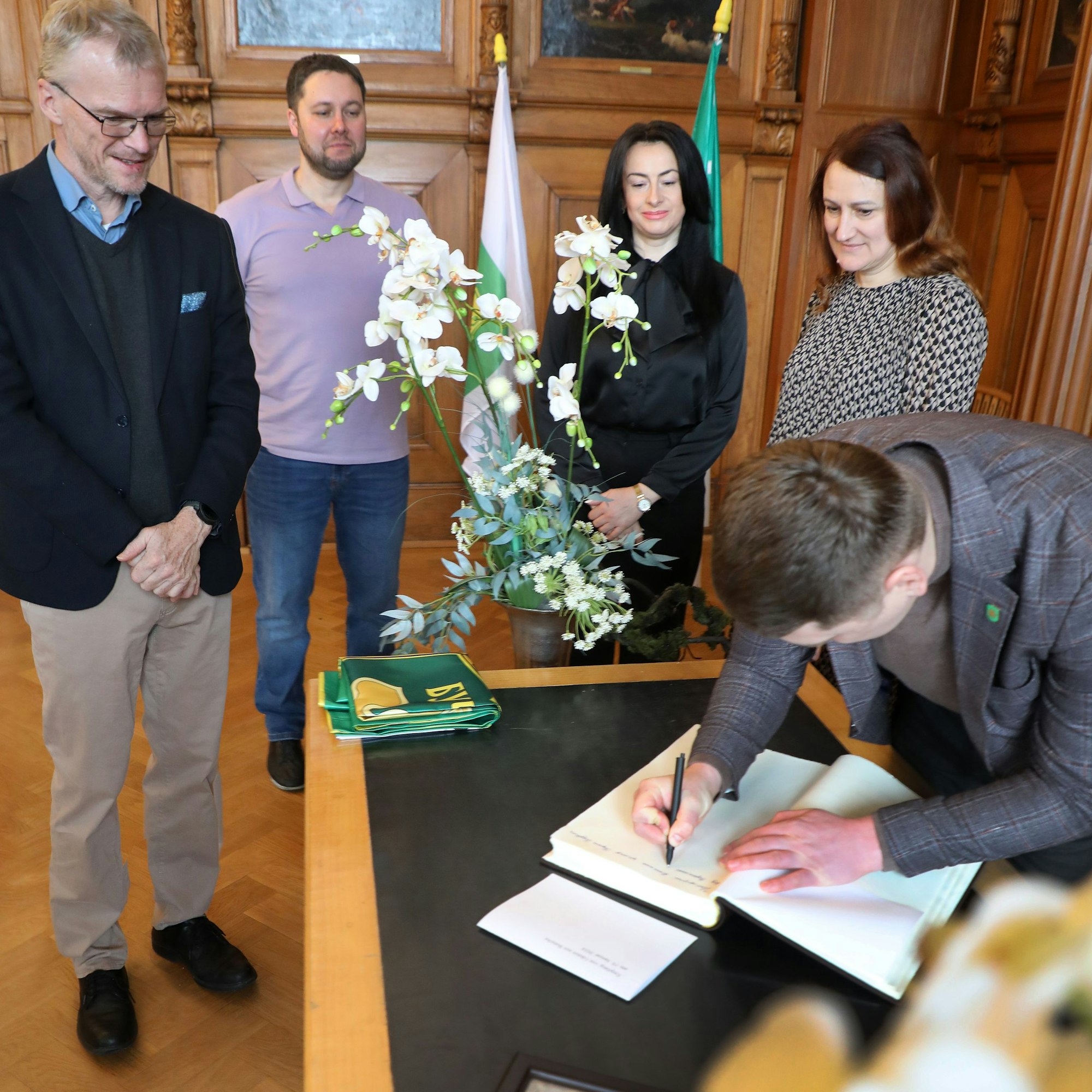 Die Delegation aus Butscha trägt sich ins Goldene Buch der Stadt Bergisch Gladbach ein. Bürgermeister Frank Stein steht daneben und freut sich.