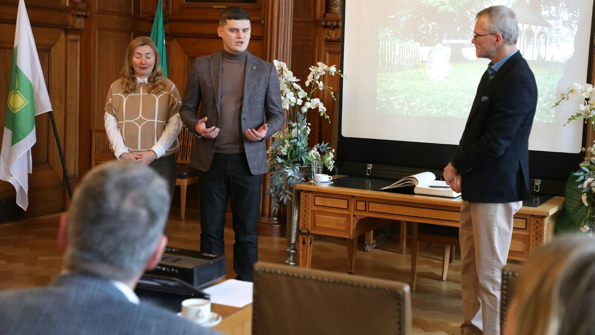Taras Shapravsky, Domletescherin Tanja Rybakova und Bergisch Gladbachs Bürgermeister Frank Stein stehen vor Publikum im Bergisch Gladbacher Ratssaal.