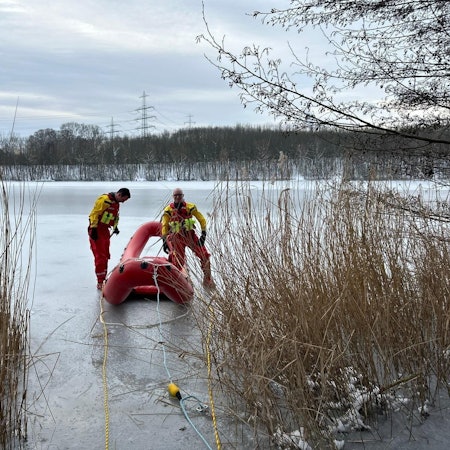 Ein Schlauchboot und zwei Feuerwehrmänner auf einem vereisten See.