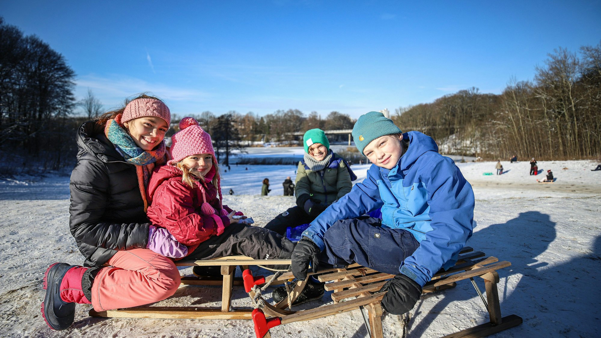 Vier Kinder auf Schlitten am Rodelhang.