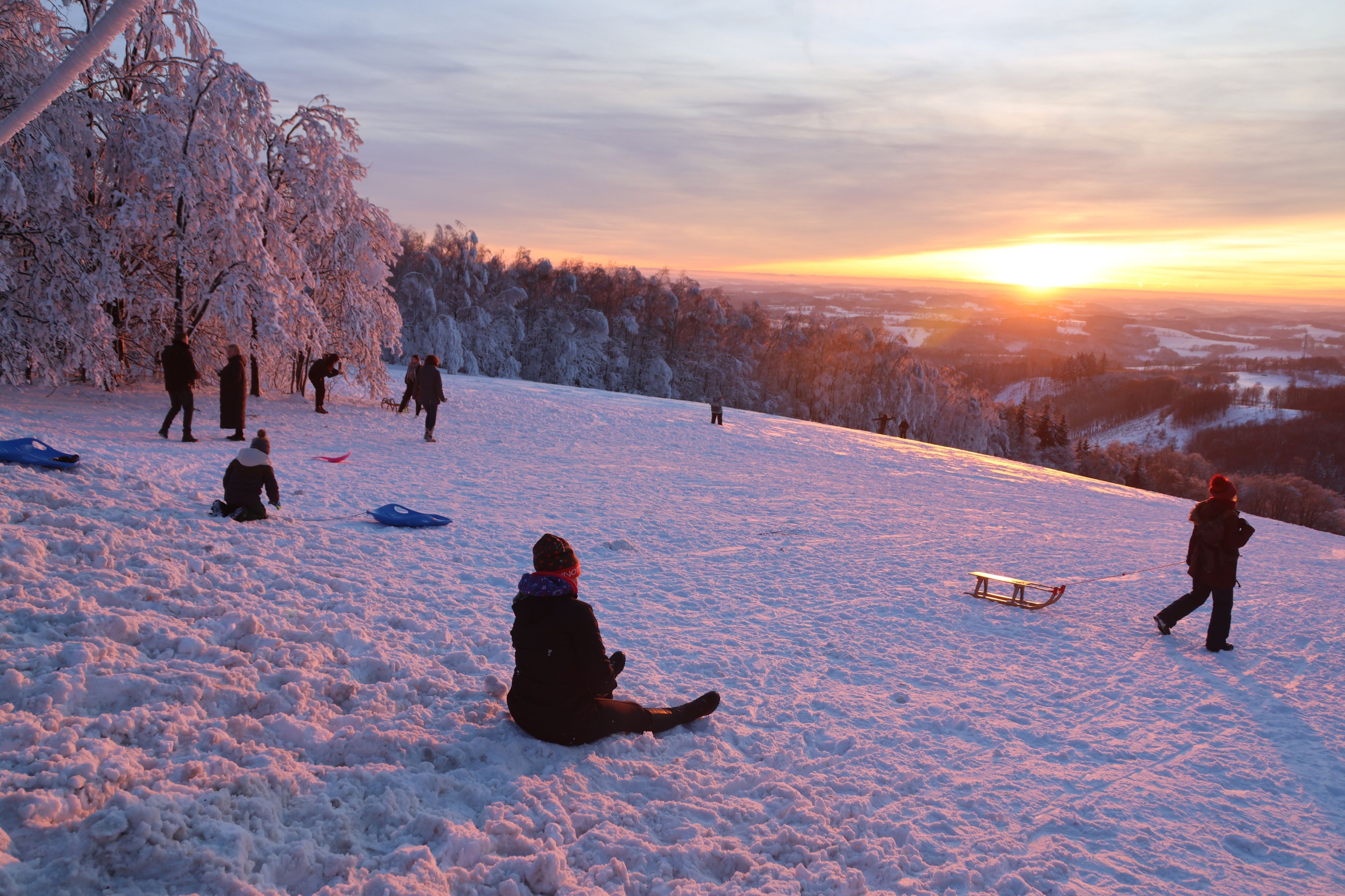 Rodelnde Kinder vor untergehender Sonne.