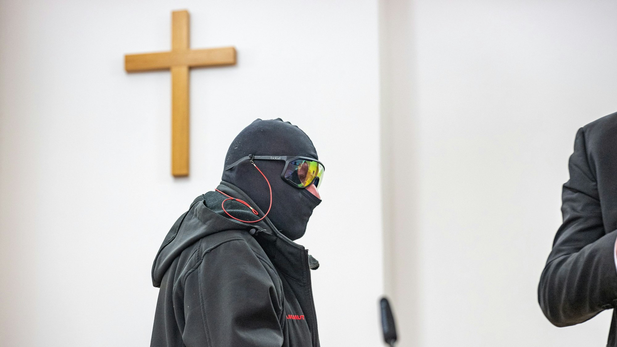 Ein Mann steht mit Sturmhaube und Sonnenbrille vermummt in einem Gerichtssaal.