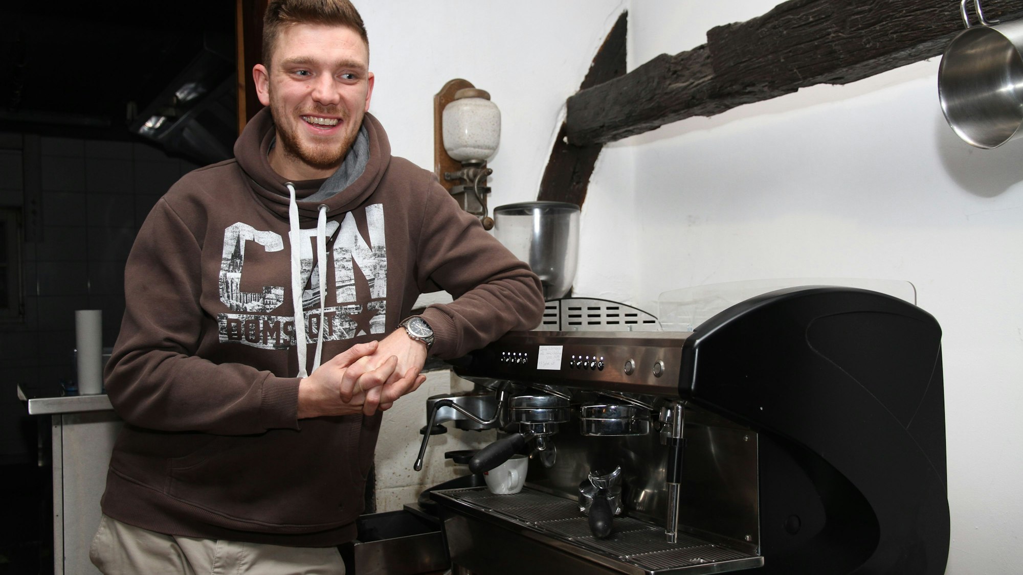 Ein Mann lehnt sich an eine große Profi-Kaffeemaschine