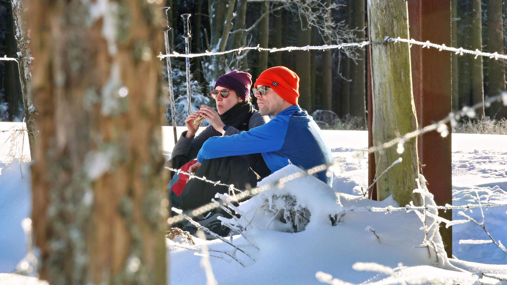 Ein Pärchen hat sich in den Schnee gesetzt, um ein Butterbrot zu essen.