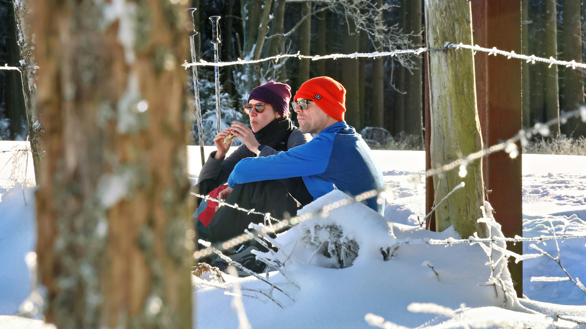 Ein Pärchen hat sich in den Schnee gesetzt, um ein Butterbrot zu essen.