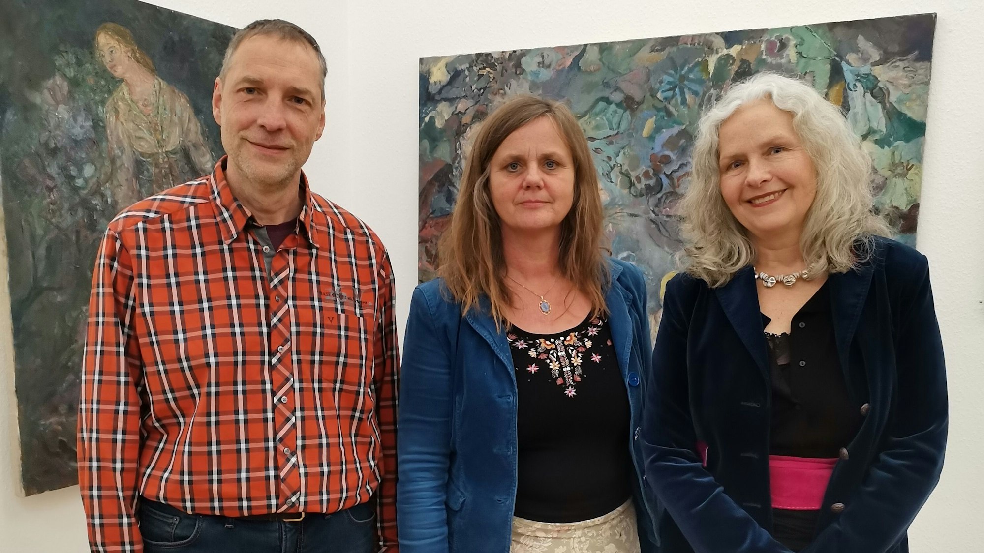 Ein Mann und zwei Frauen vor Gemälden.
