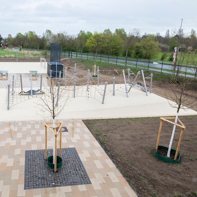 Ein frisch angelegter Schulhof mit Klettergerüst und frisch gepflanzten Bäumen ist zu sehen.
