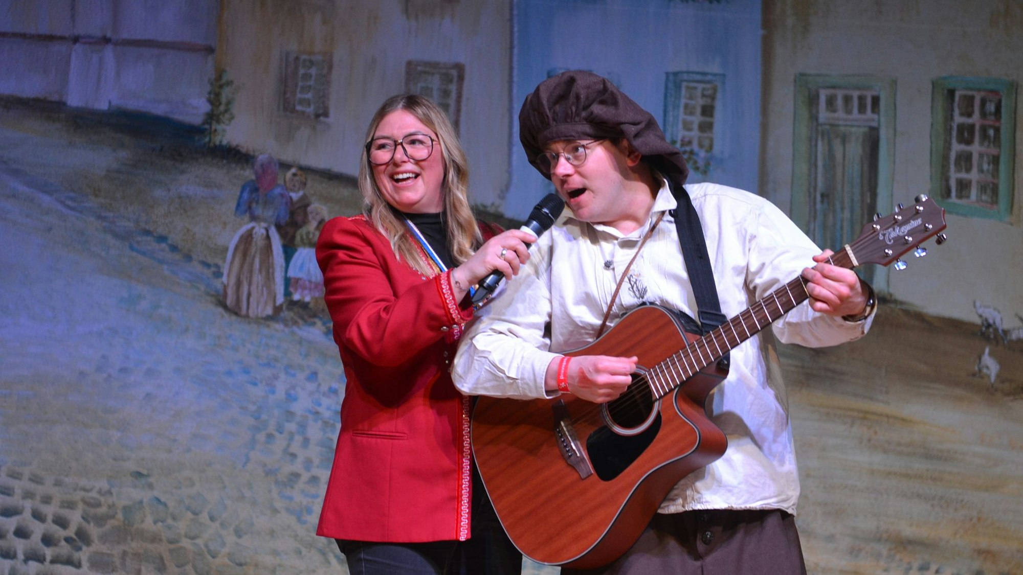 Robert Becker spielt auf der Bühne Gitarre und singt dazu, Birte Karstens hält für ihn das Mikrofon.