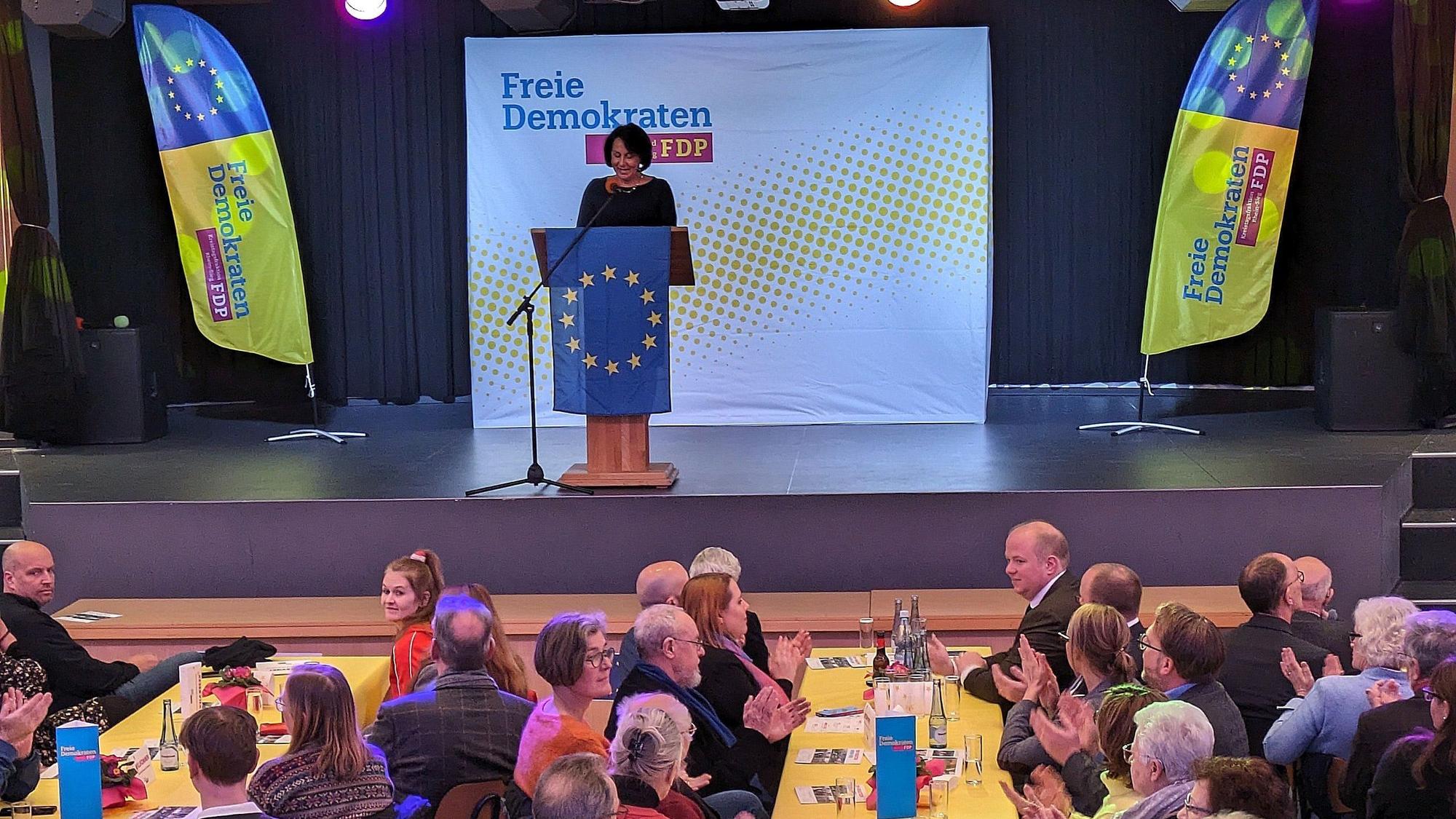 Eine Veranstaltung der FDP; auf der Bühne streht eine Frau am Rednerpult hinter einer Europafahne.