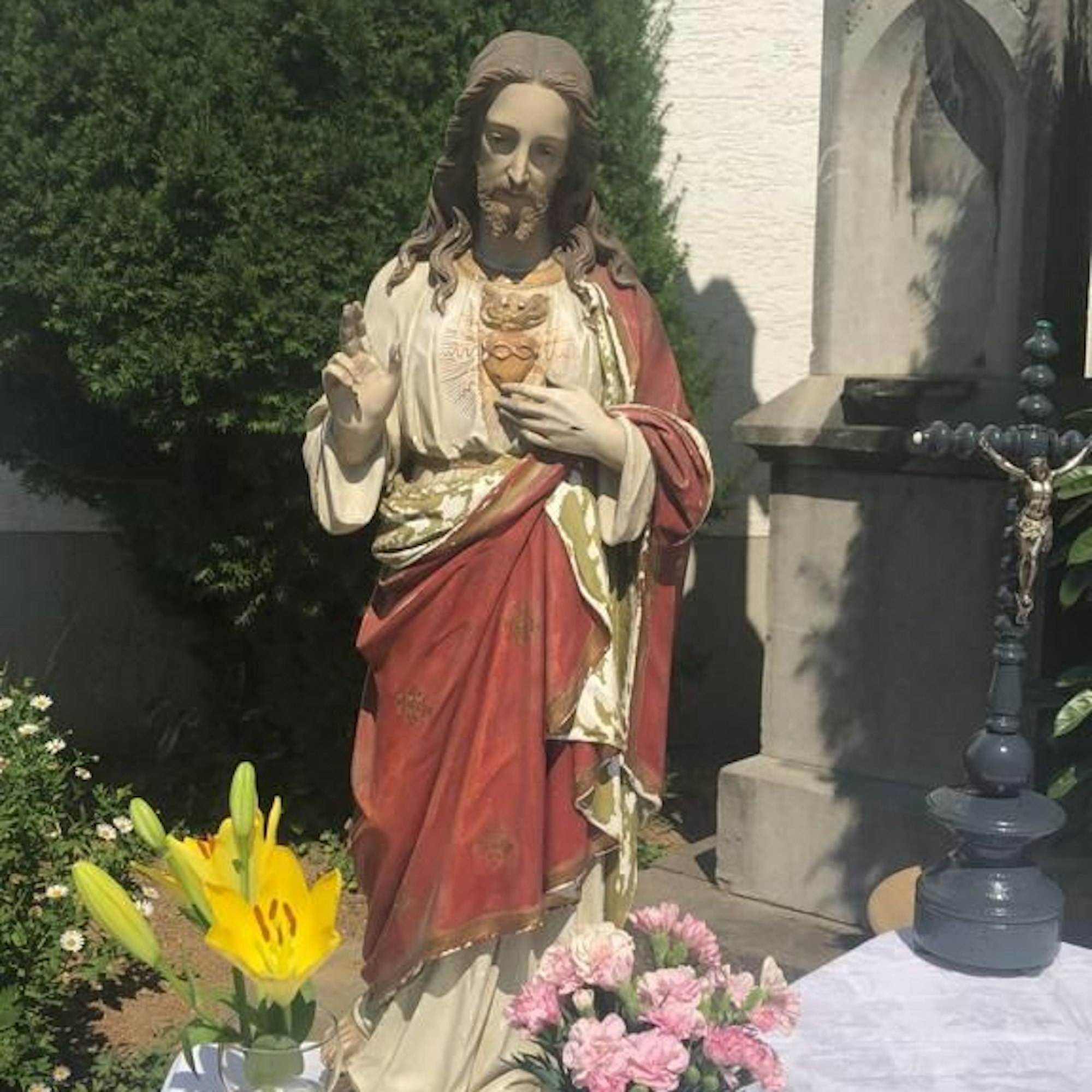 Eine Jesusfigur aus Gips mit rotem Umhang steht zwischen Blumen.