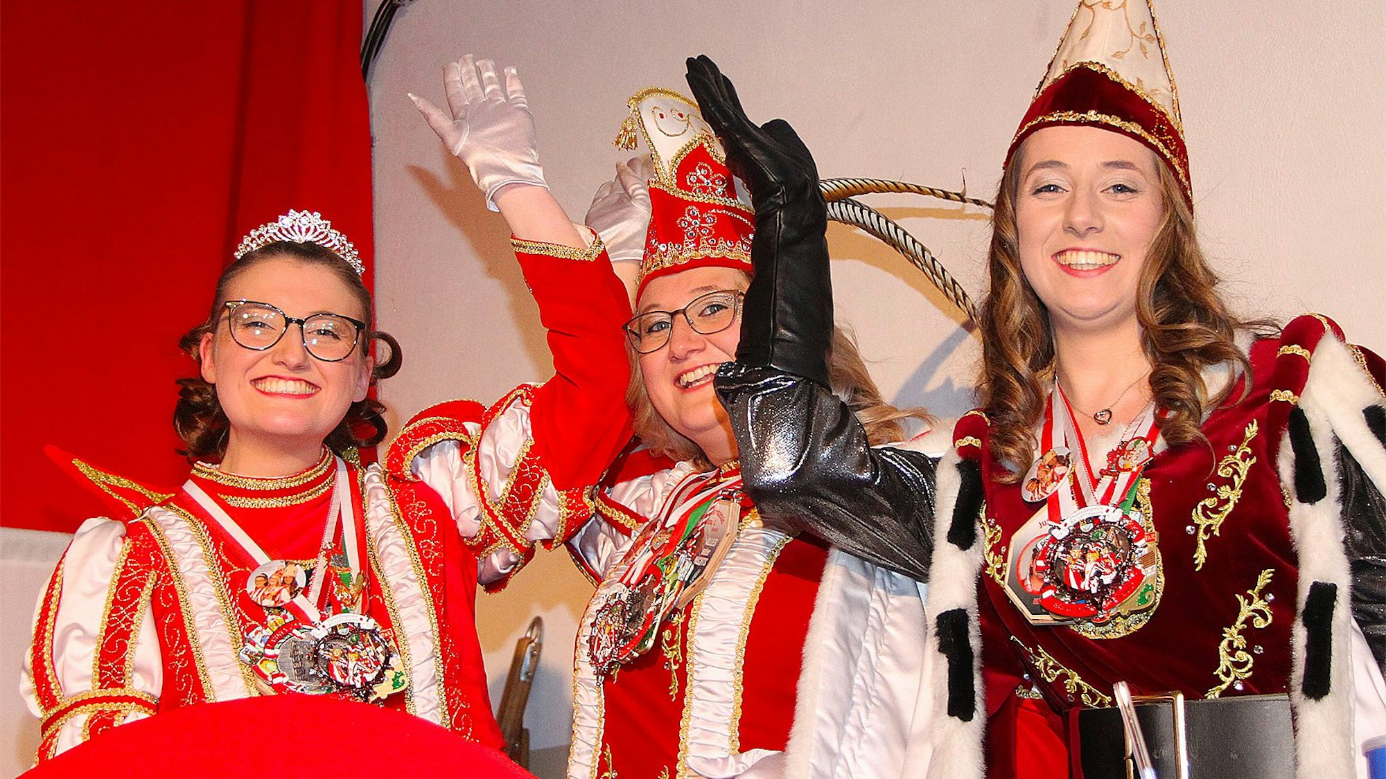 Die drei Frauen, die das Dreigestirn bilden, lachen fröhlich in die Kamera. Sie tragen jeweils mehrere Karnevalsorden.