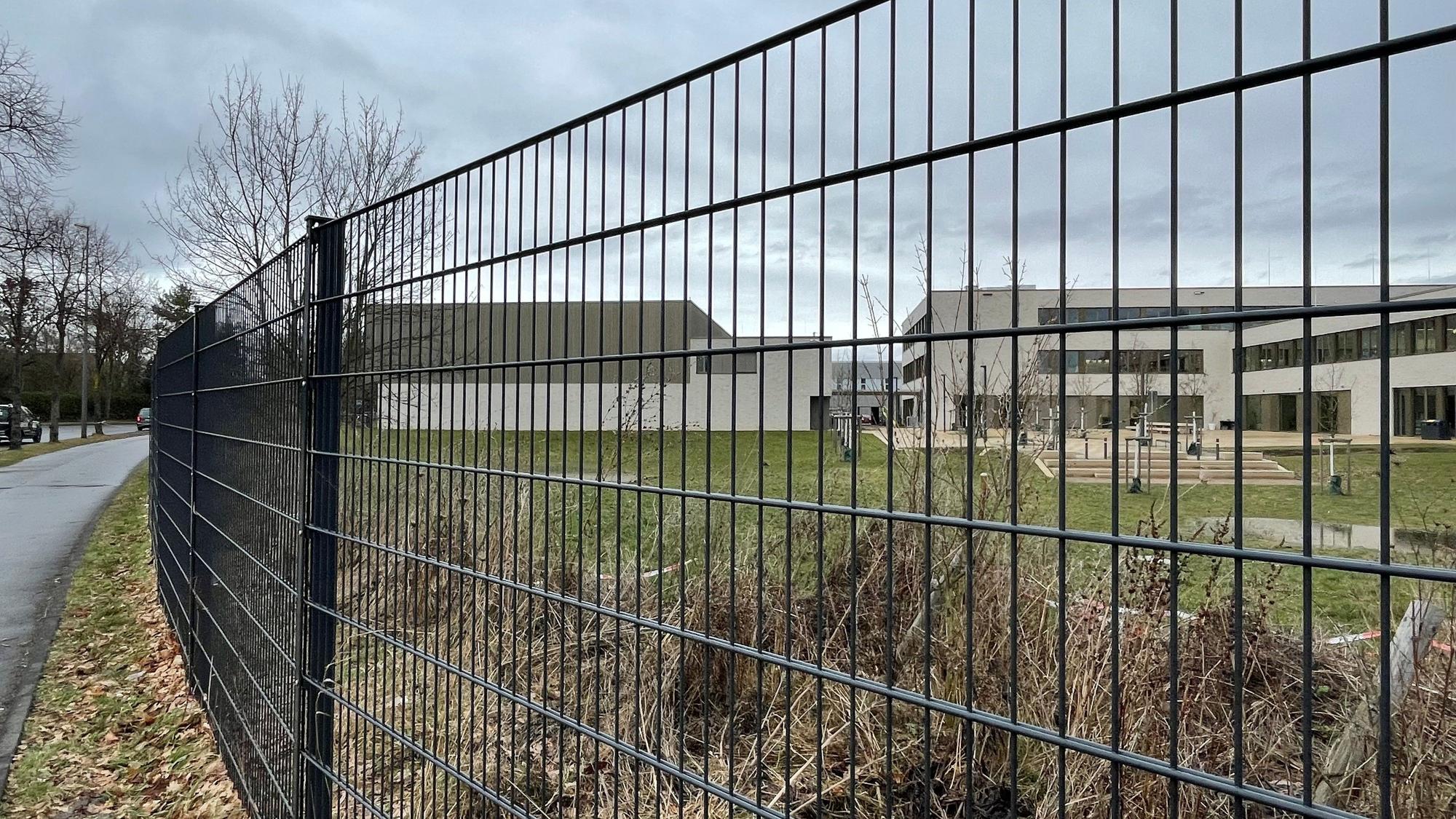 Blick durch einen Zaun auf einen Schulhof mit einer großen Rasenfläche