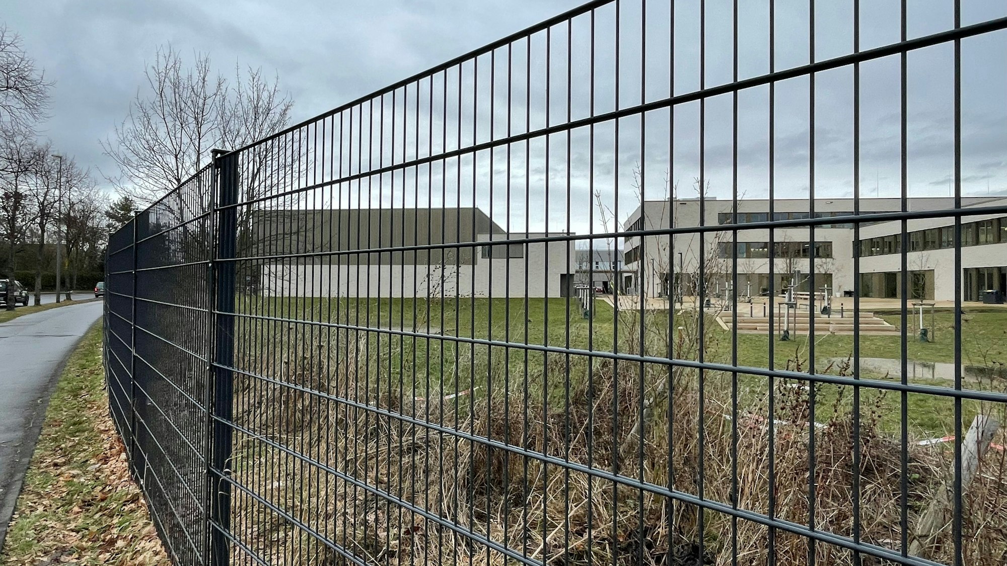 Blick durch einen Zaun auf einen Schulhof mit einer großen Rasenfläche