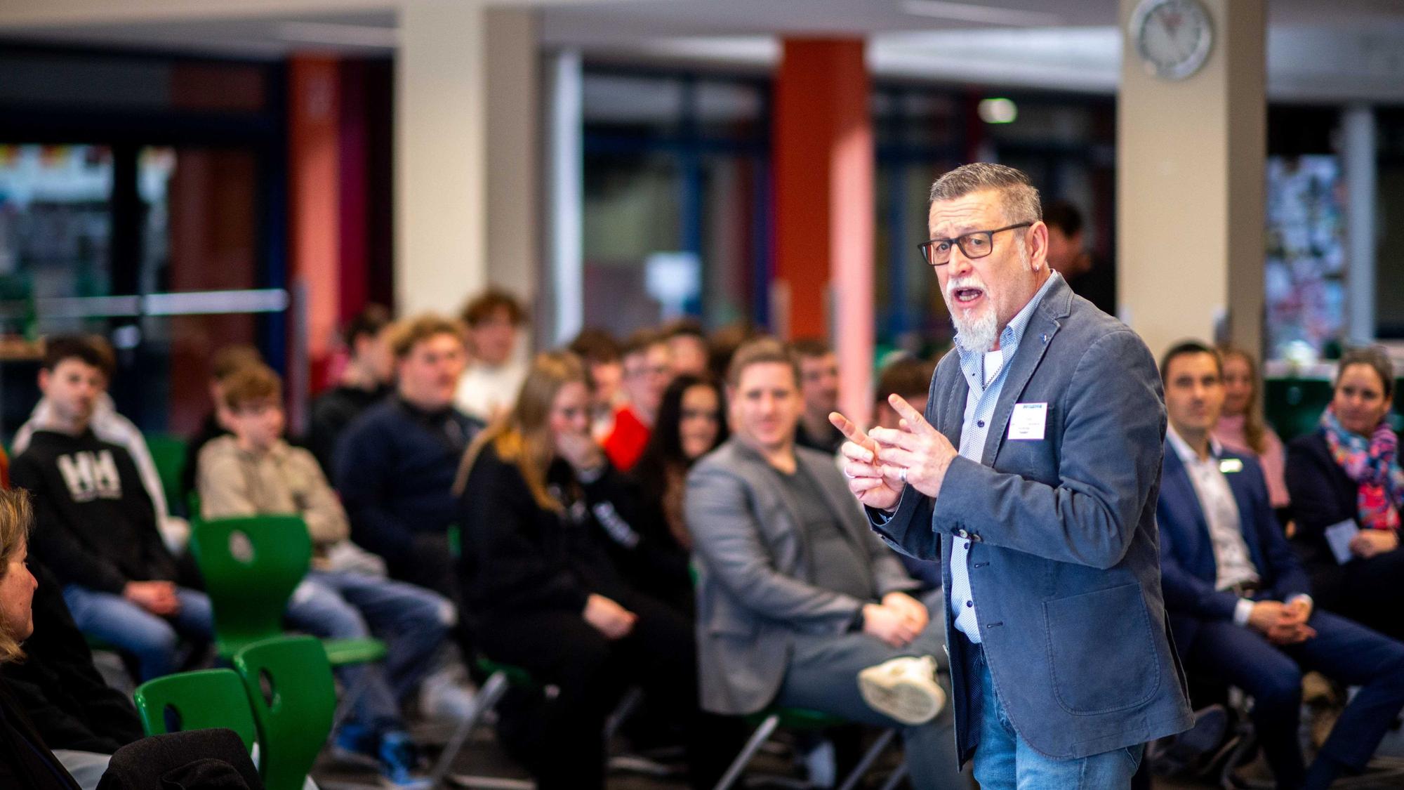 Das Bild zeigt Paul Talbot in der Mensa der Hauptschule. Er erklärt gestenreich das Projekt.