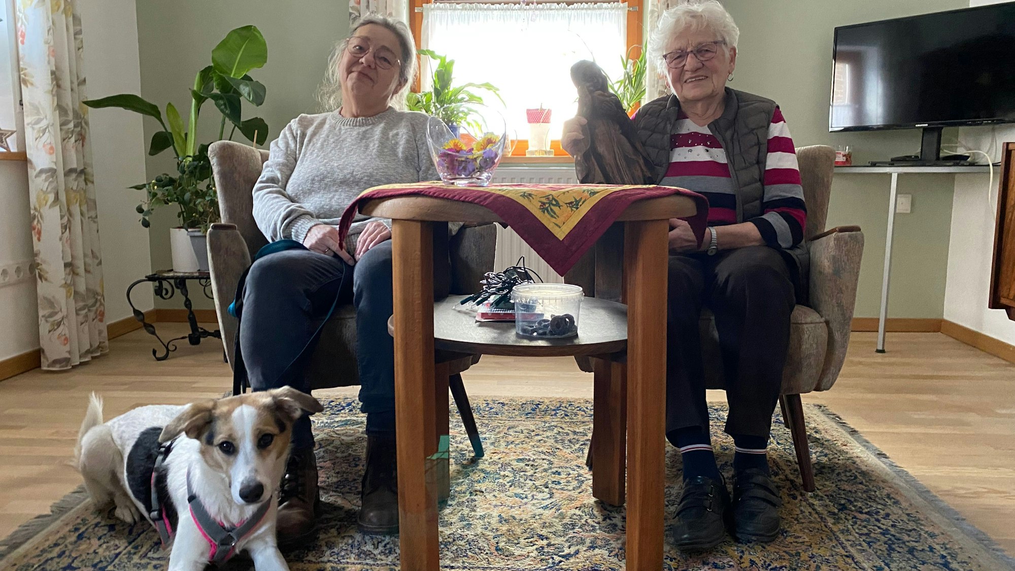 Anneliese und Gerti Jüssen (l.) sitzen an einem Tisch. Ein Hund liegt davor. Anneliese Jüssen hält eine Madonnenfigur im Arm.