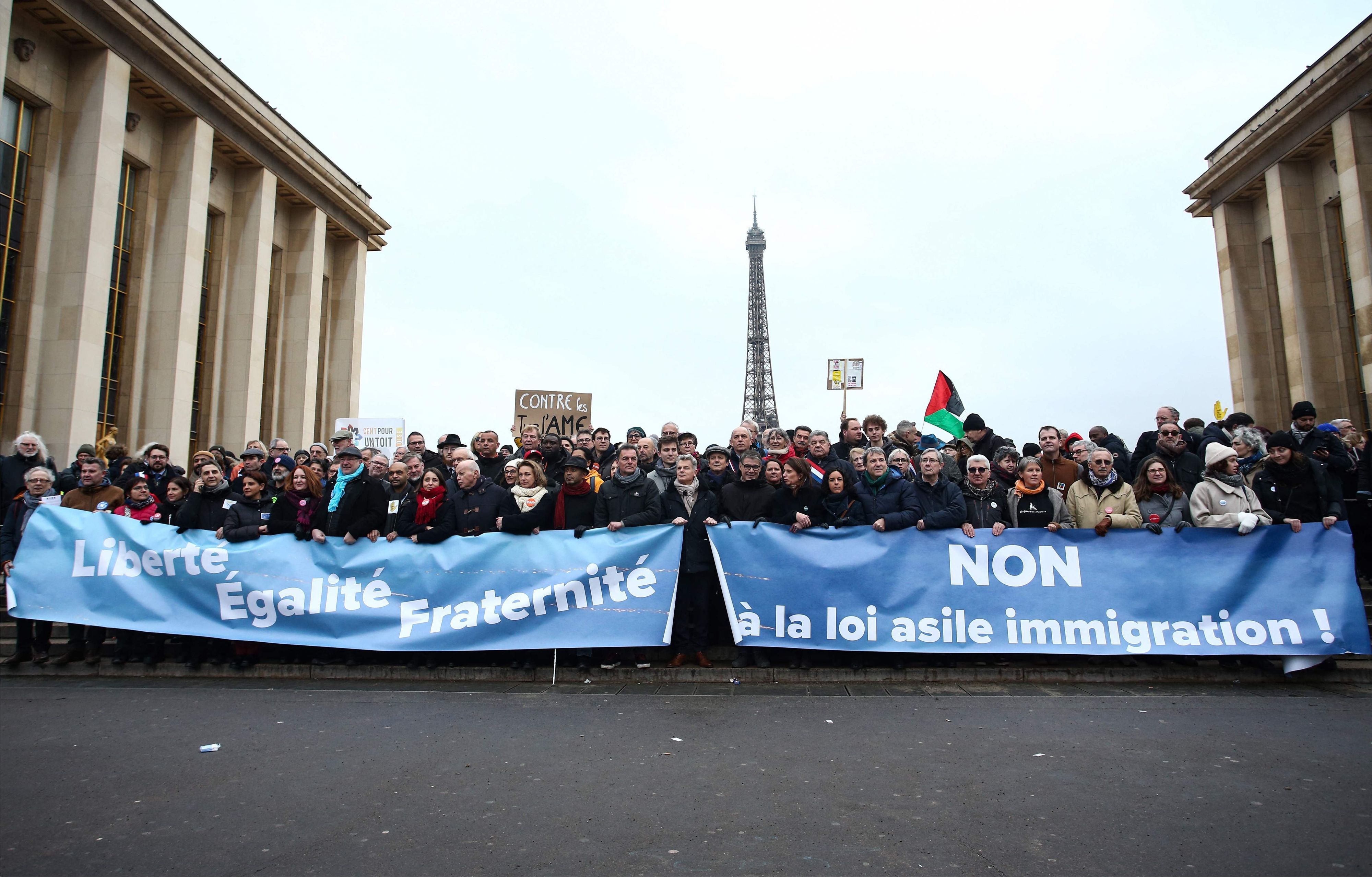 Demonstranten stehen mit Transparenten mit der Aufschrift ‚Freiheit, Gleichheit, Brüderlichkeit‘ (l) und ‚Nein zum Asyl-Einwanderungsgesetz‘ bei einer Demonstration gegen das kürzlich verabschiedete französische Einwanderungsgesetz.