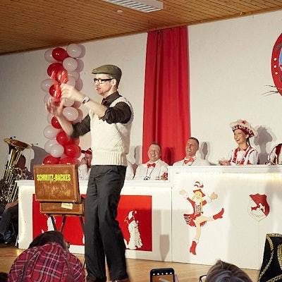 Auf der Nettersheimer Bühne produziert der Zauberer Schmitz-Backes eine Ballonfigur. Sein Publikum lacht.
