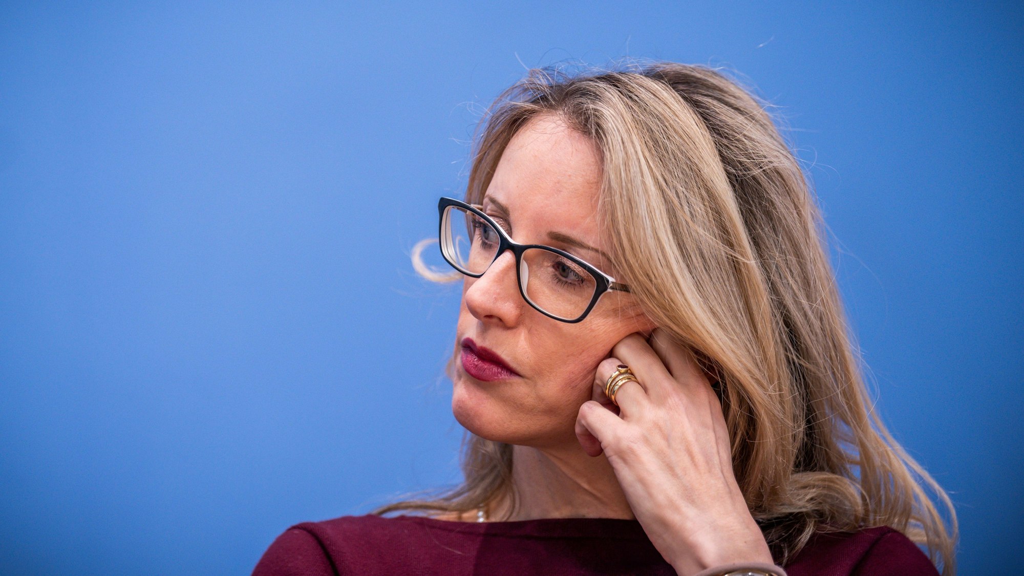 Alena Buyx sitzt vor einem blauen Hintergrund und hat den Kopf zur Seite gedreht und auf einer Hand abgestützt.