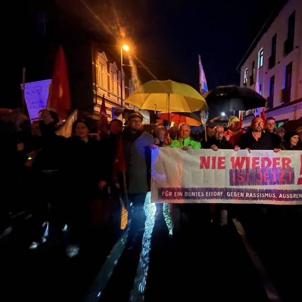 Menschen mit einem großen Plakat gehen einem Demonstrationszug vorweg.