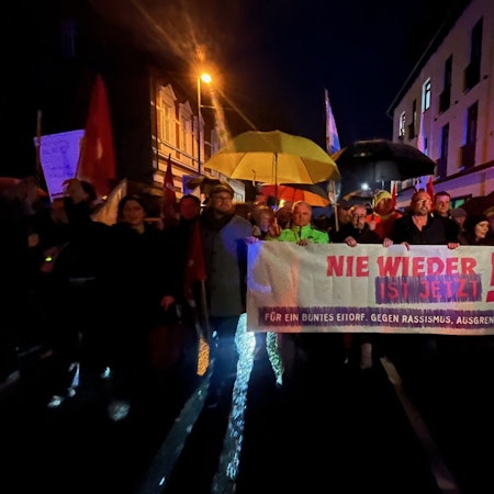 Menschen mit einem großen Plakat gehen einem Demonstrationszug vorweg.