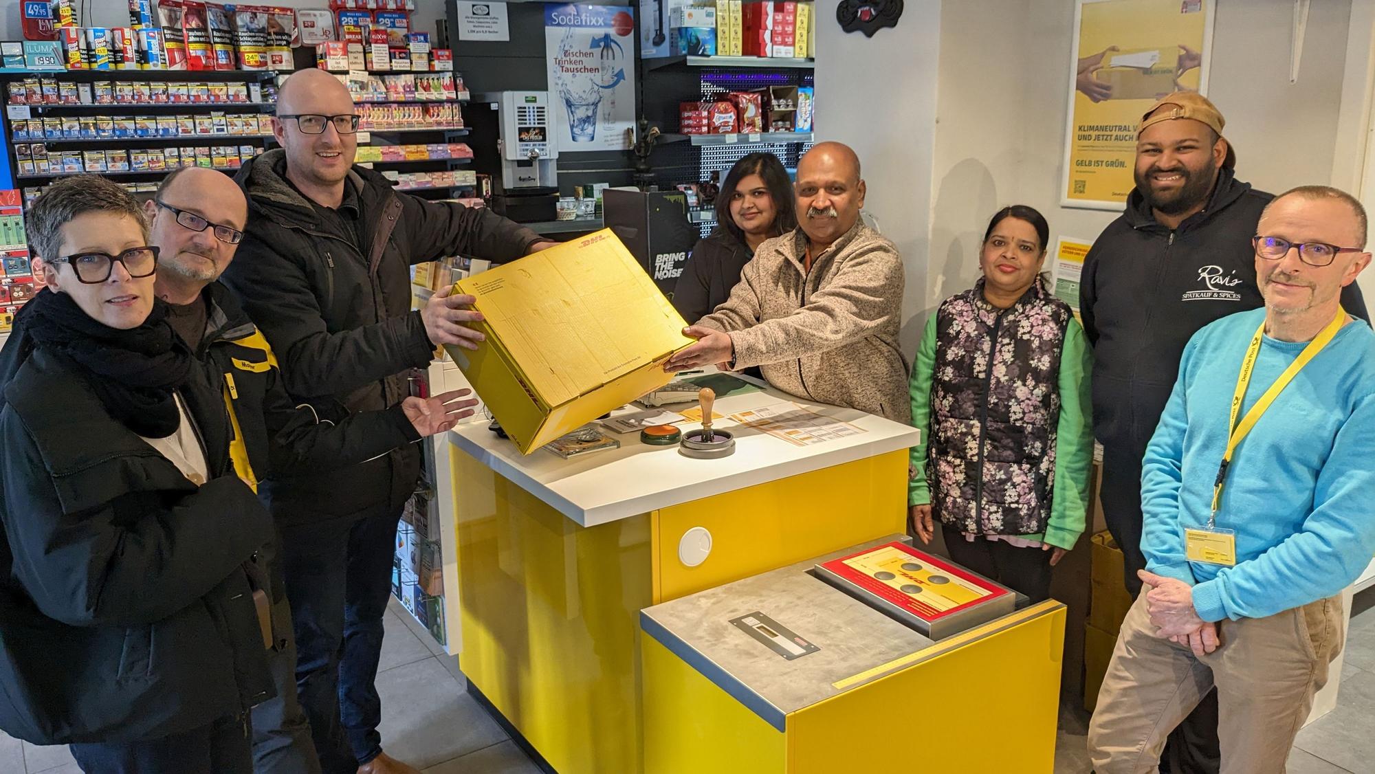 Bürgermeister Ingo Pfennings liefert im Beisein weiterer Mitarbeiter das erste Postpaket in der neuen Gemünder Postagentur bei Nithiyanandasivam Ravichandran ein.