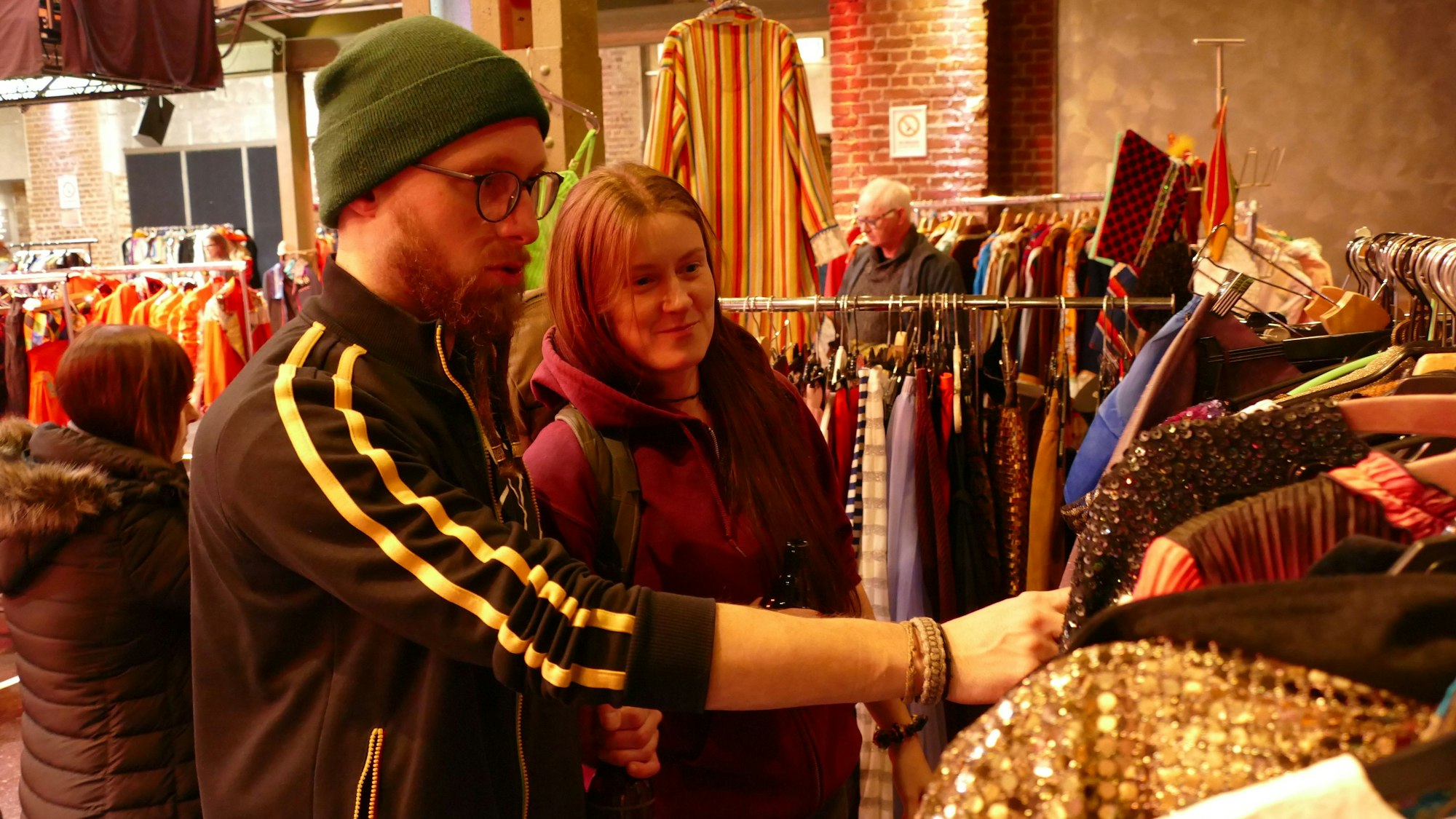 Ein Mann und eine Frau suchen zwischen Kleidungsstücke an einer Stange.