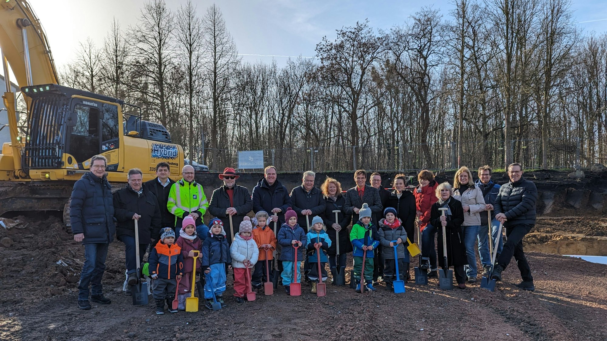 Eine Gruppe von Kindern mit Schaufeln und Erwachsenen mit Spaten auf einer Baustelle.