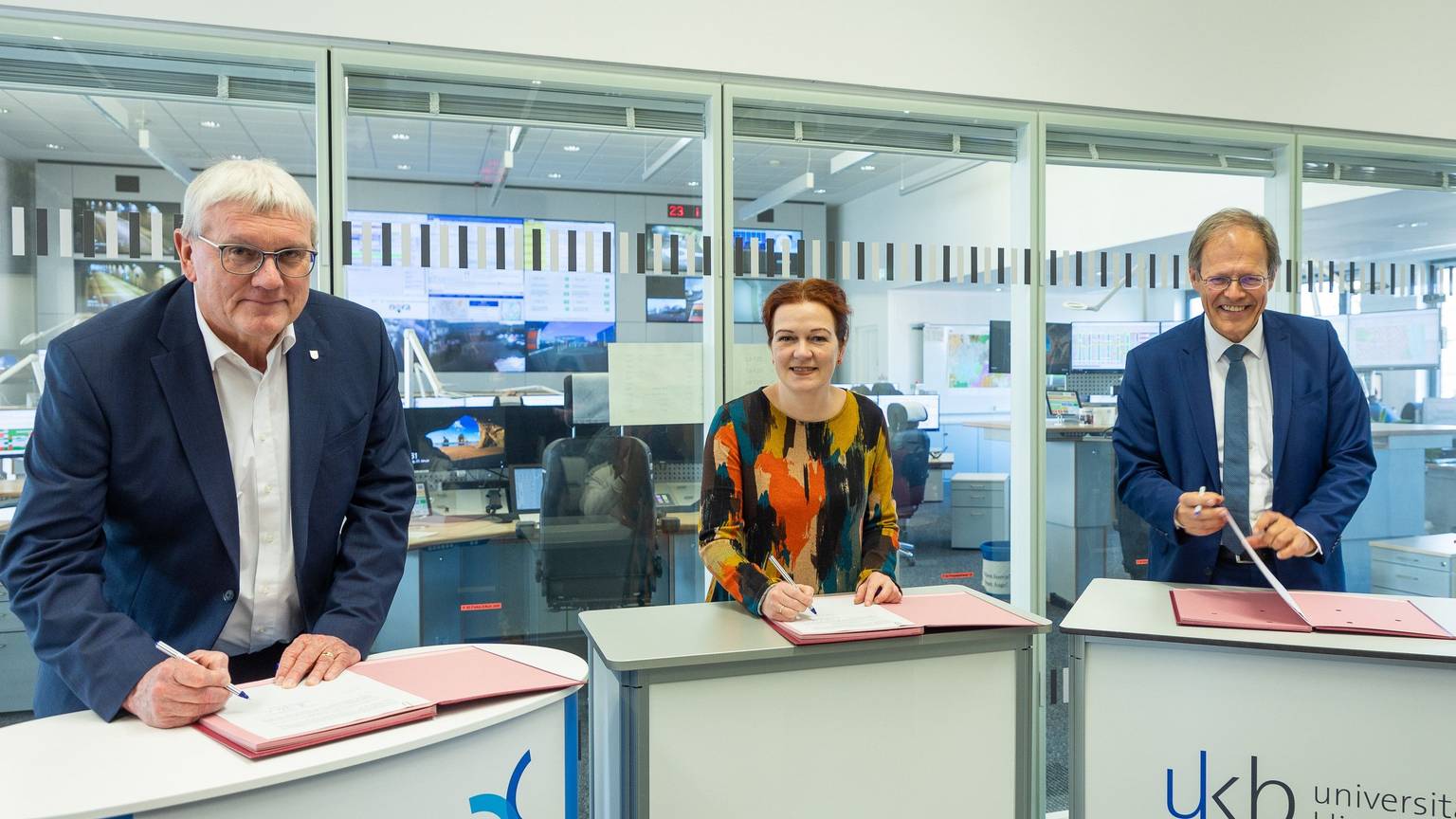 Landrat Sebastian Schuster, Bonns Oberbürgermeisterin Katja Dörner und Prof. Wolfgang Holzgreve, Ärztlicher Direktor des Universitätsklinikums Bonn (UKB), stehen in der Bonner Feuerwache 1 an Pulten und unterschreiben eine gemeinsame Vereinbarung.