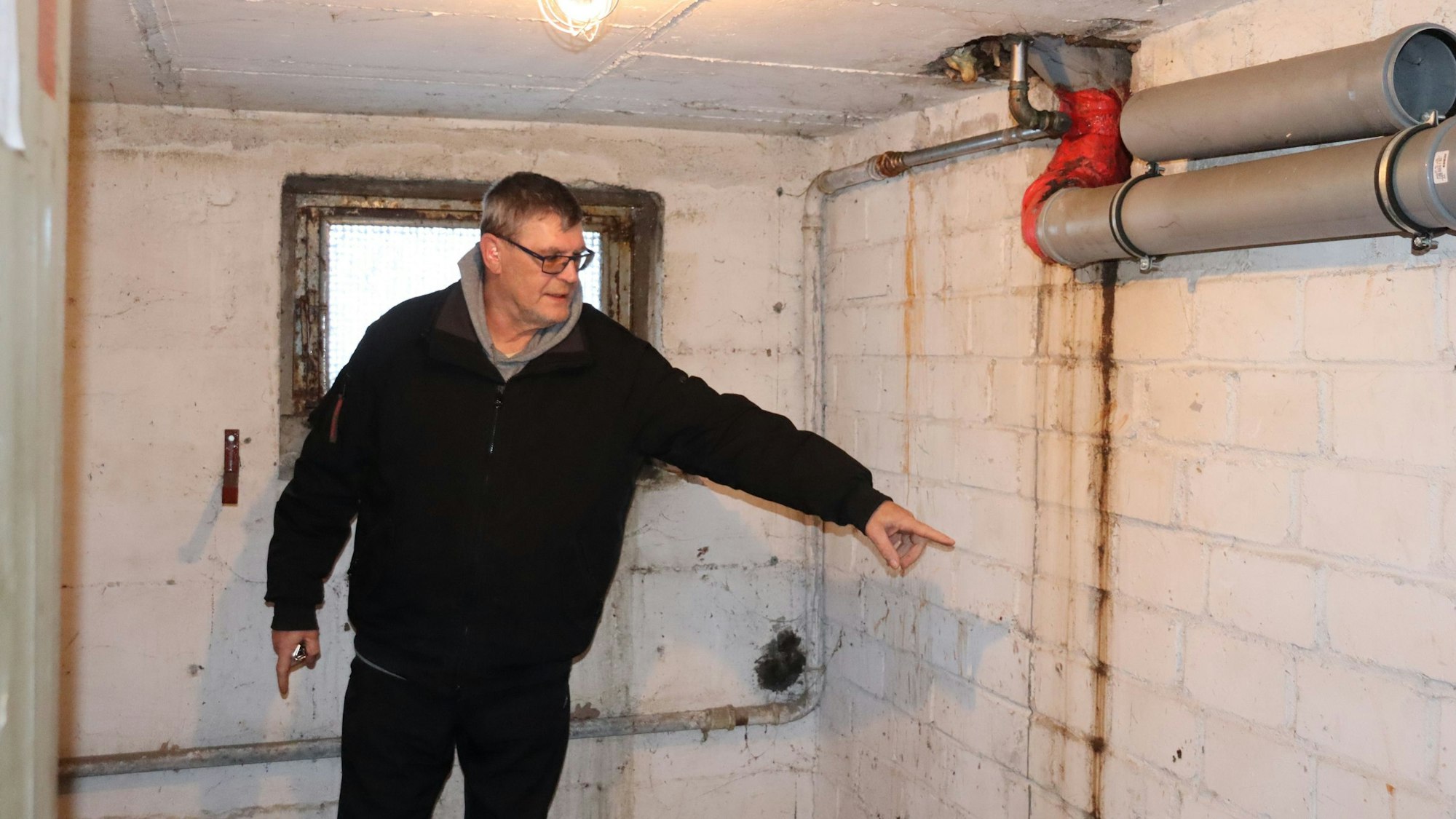 Ein Mann zeigt auf eine braune Spur an einer Kellerwand.