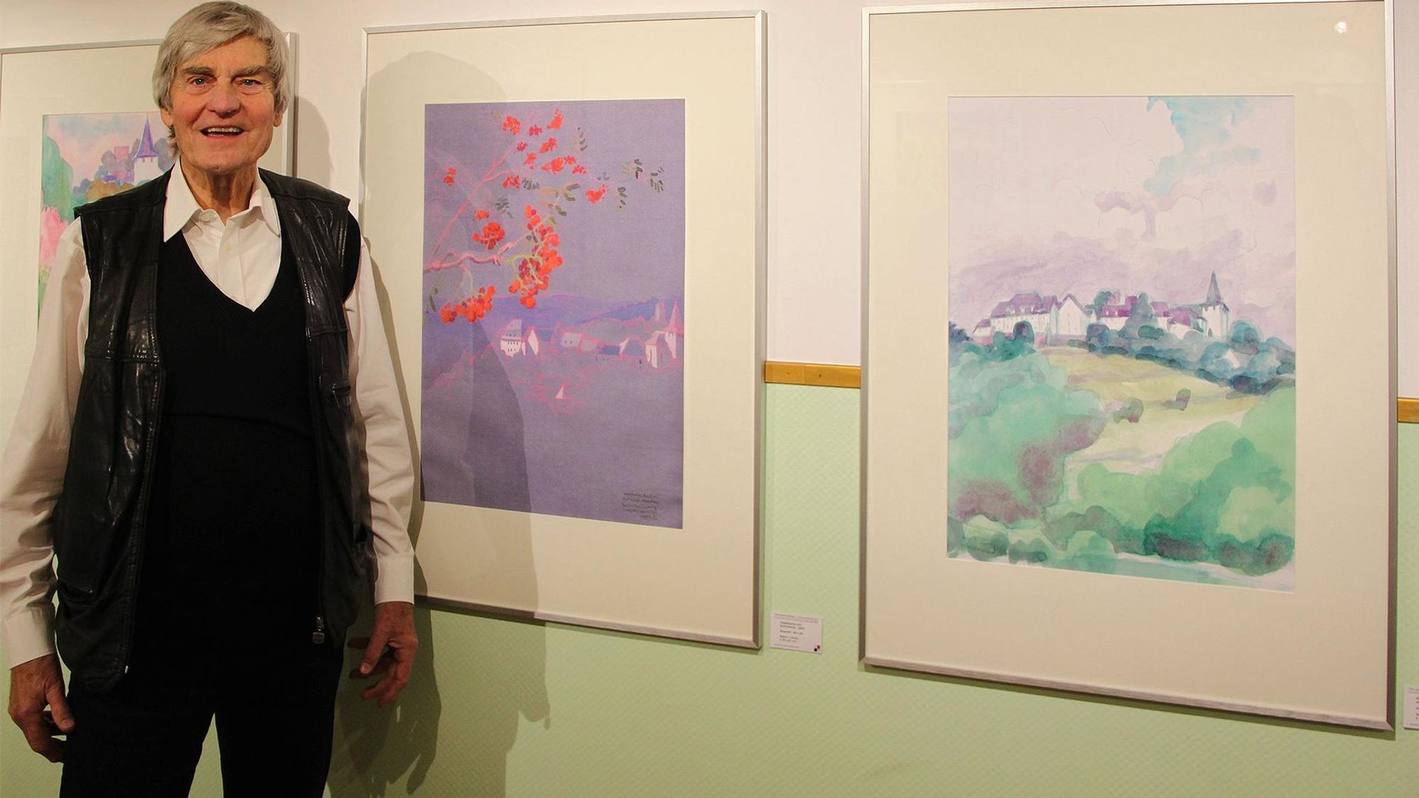 Der Kunstprofessor Hans Günter Hoffmann steht neben zwei Aquarellen von Kronenburg.