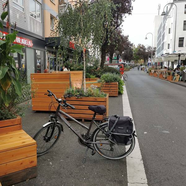 Auf einem Parkstreifen stehen Holzkübel mit Blume und Sitzmöglichkeiten.