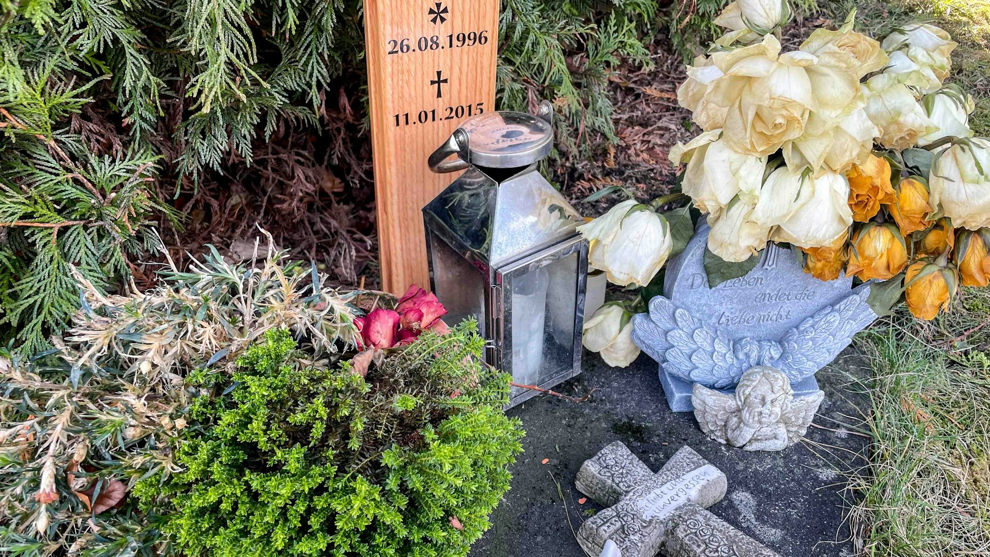 Das Bild zeigt den Gedenkort einer jungen Frau, die in Euskirchen bei einem Verkehrsunfall ums Leben gekommen ist. Vor dem Kreuz stehen Kerze und Blumen.
