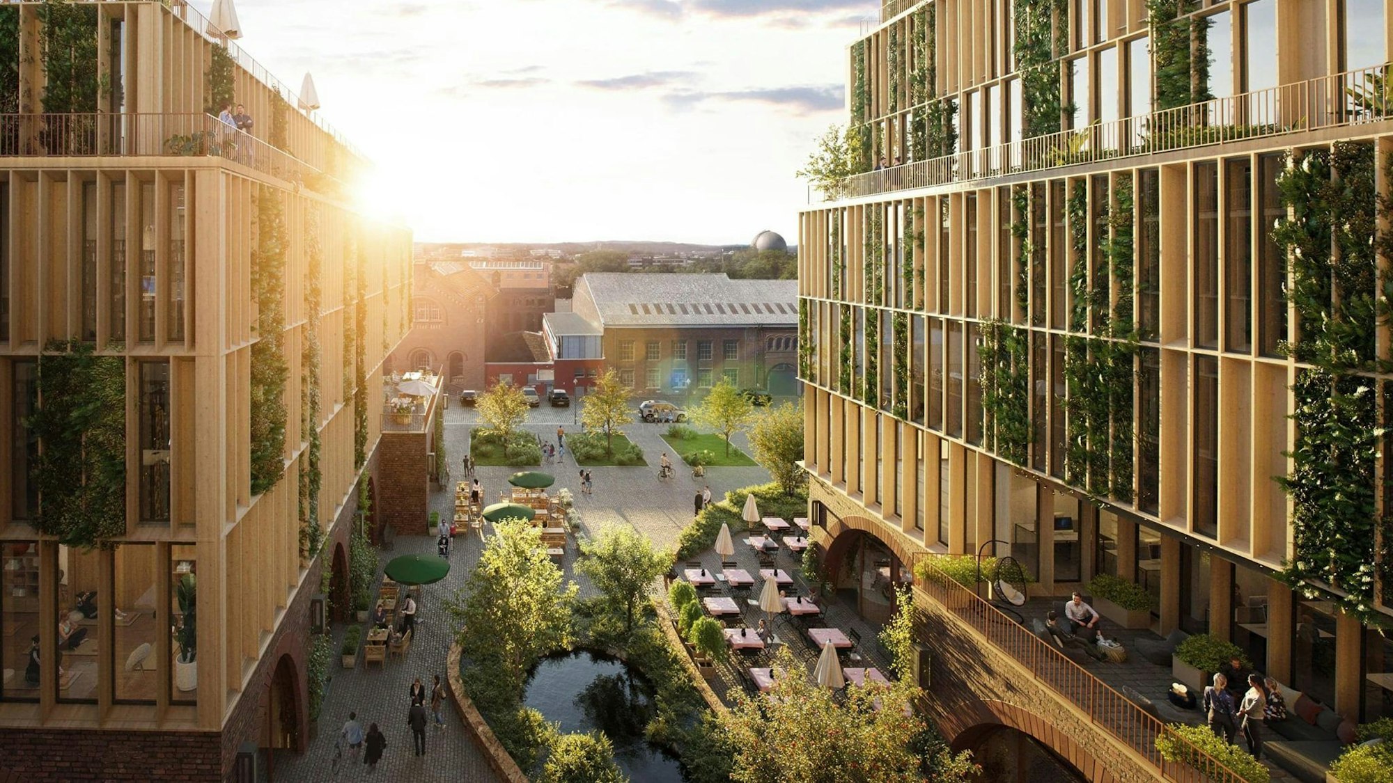 Zwei Gebäudekomplexe mit einer Grünanlage mit Teich und dem Außenbereich einer Gastronomie sind zu sehen.