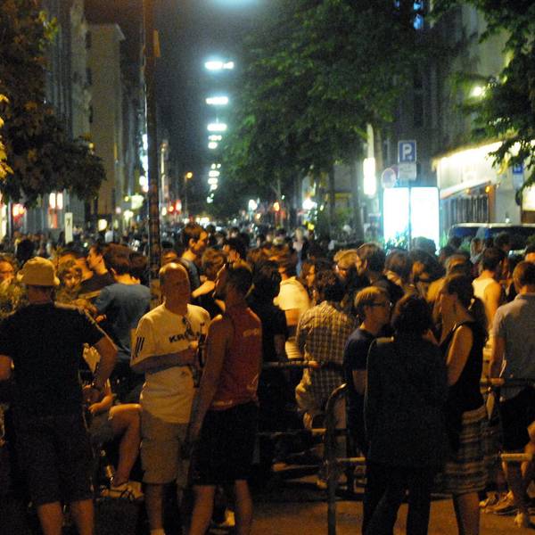Viele Menschen stehen bei sommerlichen Temperaturen zusammen auf der Straße.