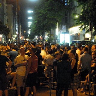 Viele Menschen stehen bei sommerlichen Temperaturen zusammen auf der Straße.