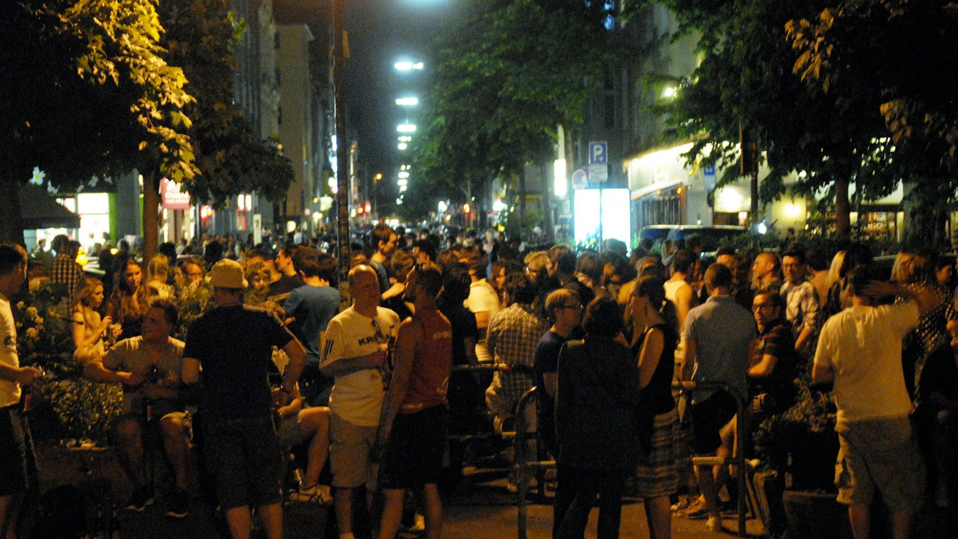 Viele Menschen stehen bei sommerlichen Temperaturen zusammen auf der Straße.