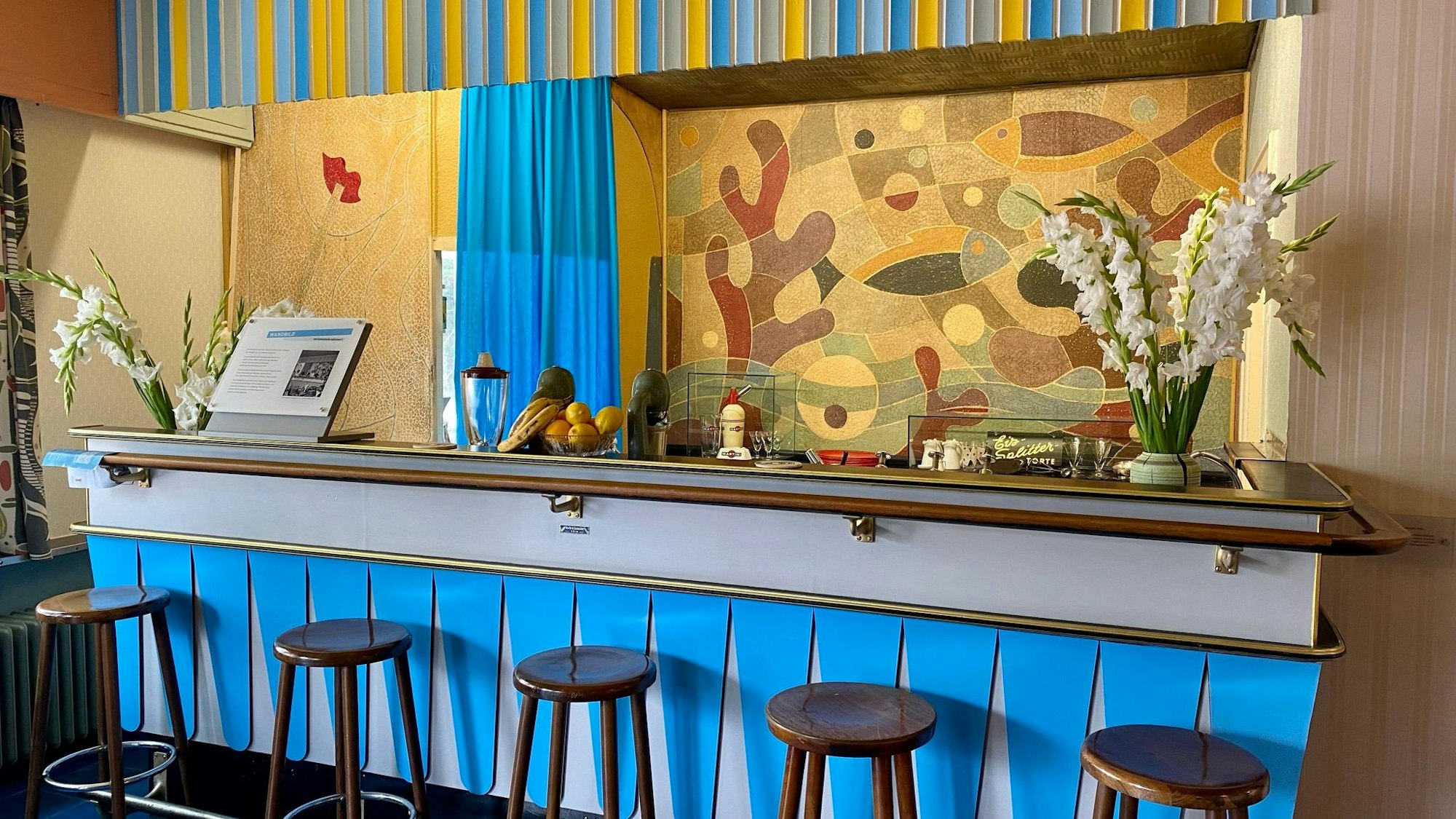 Hinter der Theke einer Milchbar ist ein Wandgemälde aus den 1950-er Jahren zu sehen.