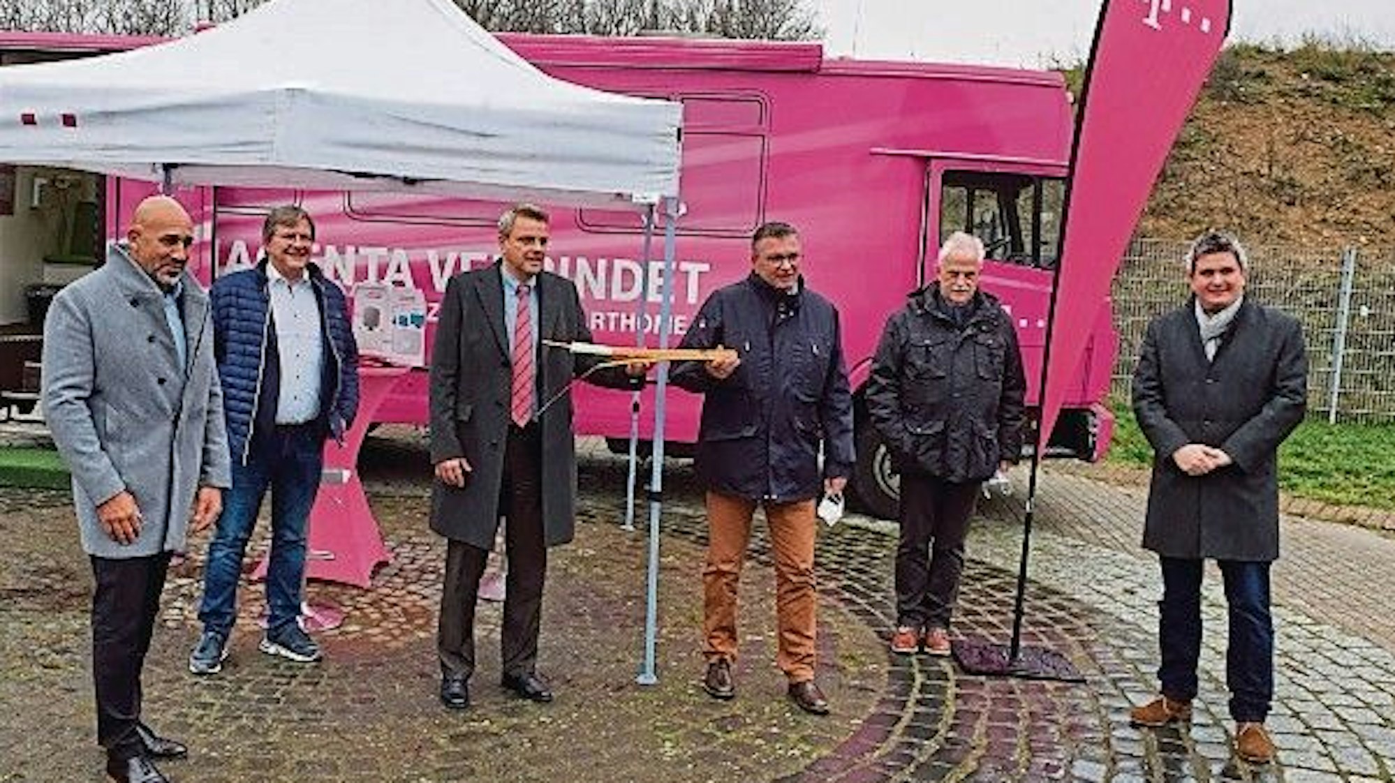 Der damalige Niederkasseler Bürgermeister Stephan Vehreschild und Vertreter von Telekom, Politik und Stadtverwaltung stehen vor einem magentafarbenen Infomobil der Telekom.