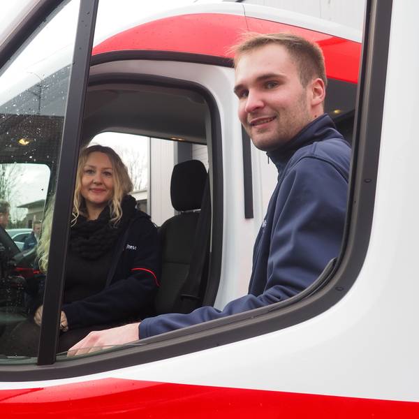 Eine Frau sitzt am Steuer eines Autos, ein Mann steht an der Tür.