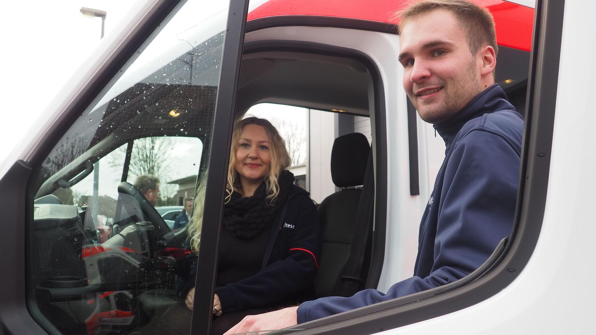 Eine Frau sitzt am Steuer eines Autos, ein Mann steht an der Tür.