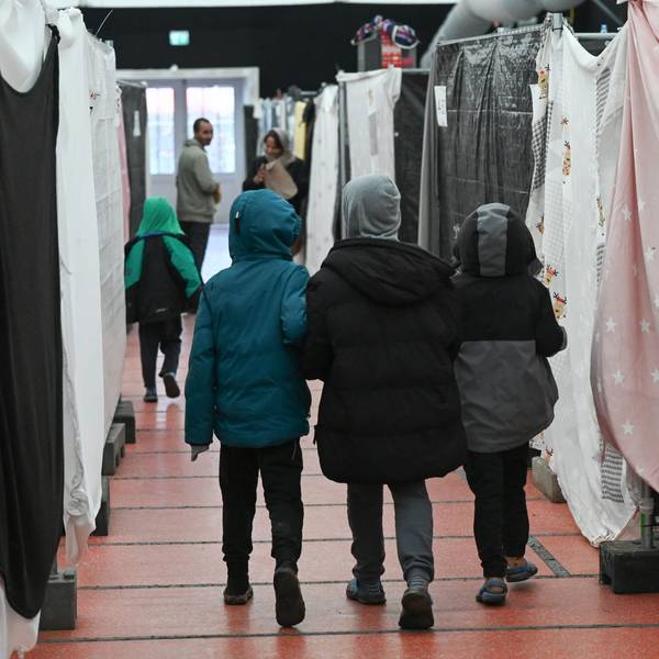 Das Symbolbild zeigt Kinder von hinten, die durch eine Geflüchtetenunterkunft gehen.