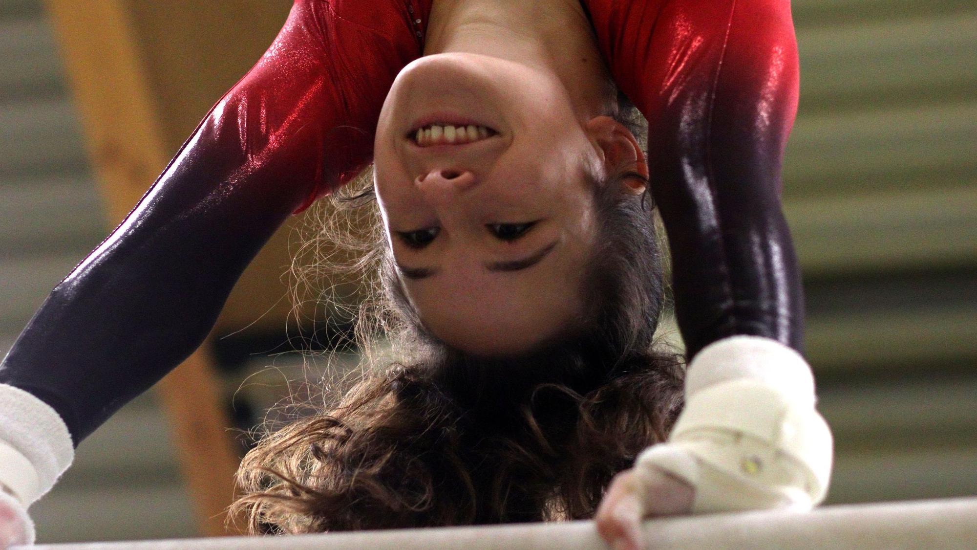 Anouk Hauser lächelt, während sie einen Handstand am Reck macht.