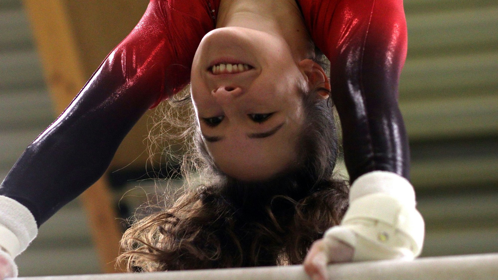 Anouk Hauser lächelt, während sie einen Handstand am Reck macht.