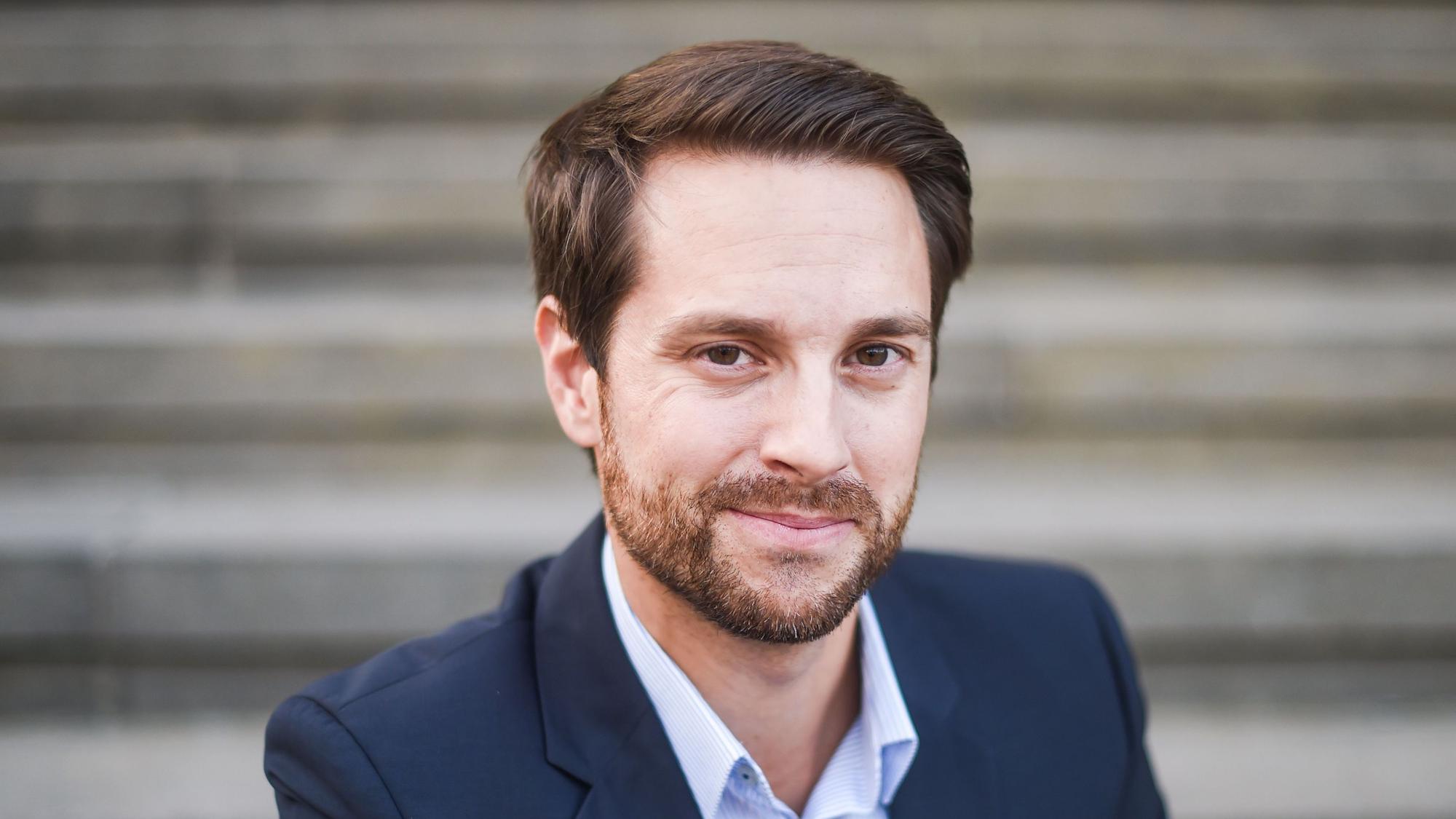 Mirko Drotschmann, Betreiber des Youtubekanals „MrWissen2go“, blickt in einem Anzug in die Kamera.