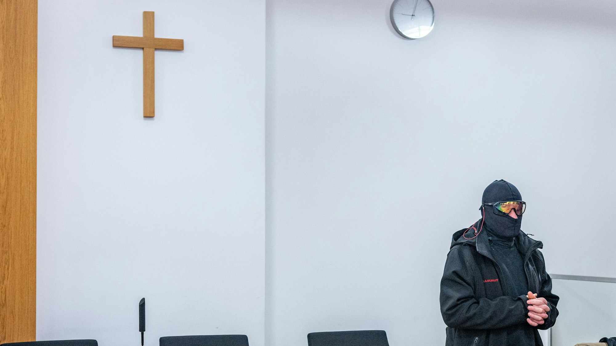 Der Priester im Gerichtsaal. Er trägt eine Sturmhaube und eine Skibrille.