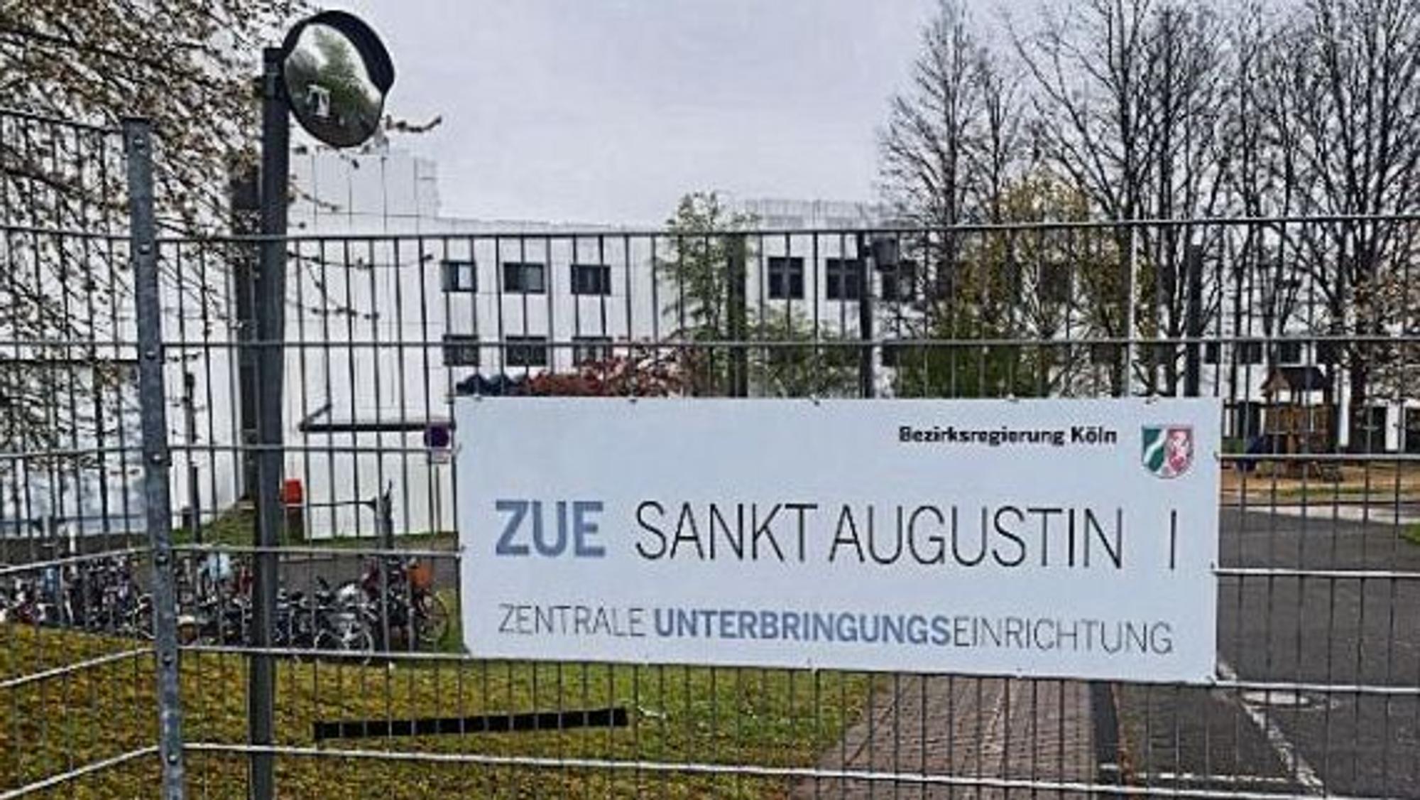 Ein Schild an einem Zaun weist auf dem Gelände an der Heerstraße in Sankt Augustin auf die Zentrale Unterbringungseinrichtung (ZUE) hin.