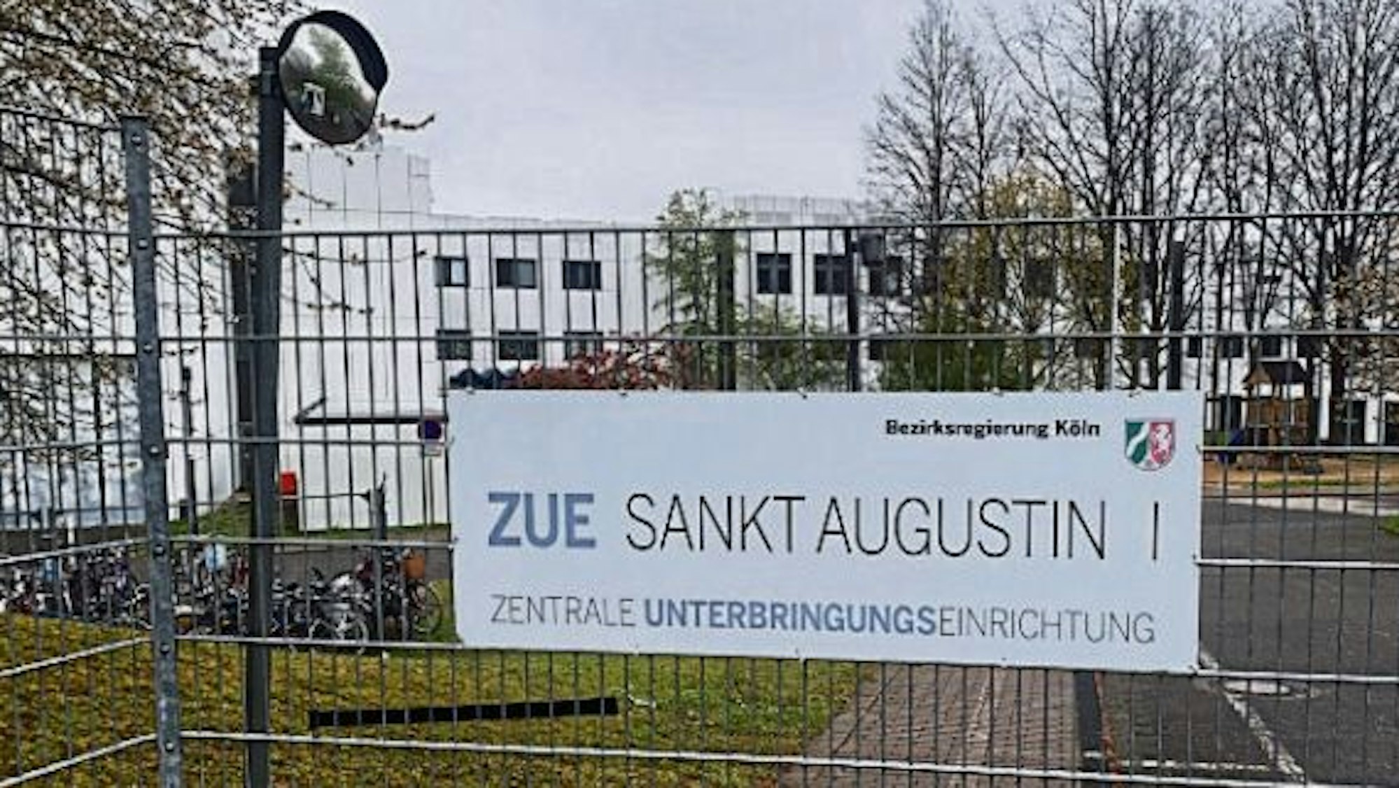 Ein Schild an einem Zaun weist auf dem Gelände an der Heerstraße in Sankt Augustin auf die Zentrale Unterbringungseinrichtung (ZUE) hin.