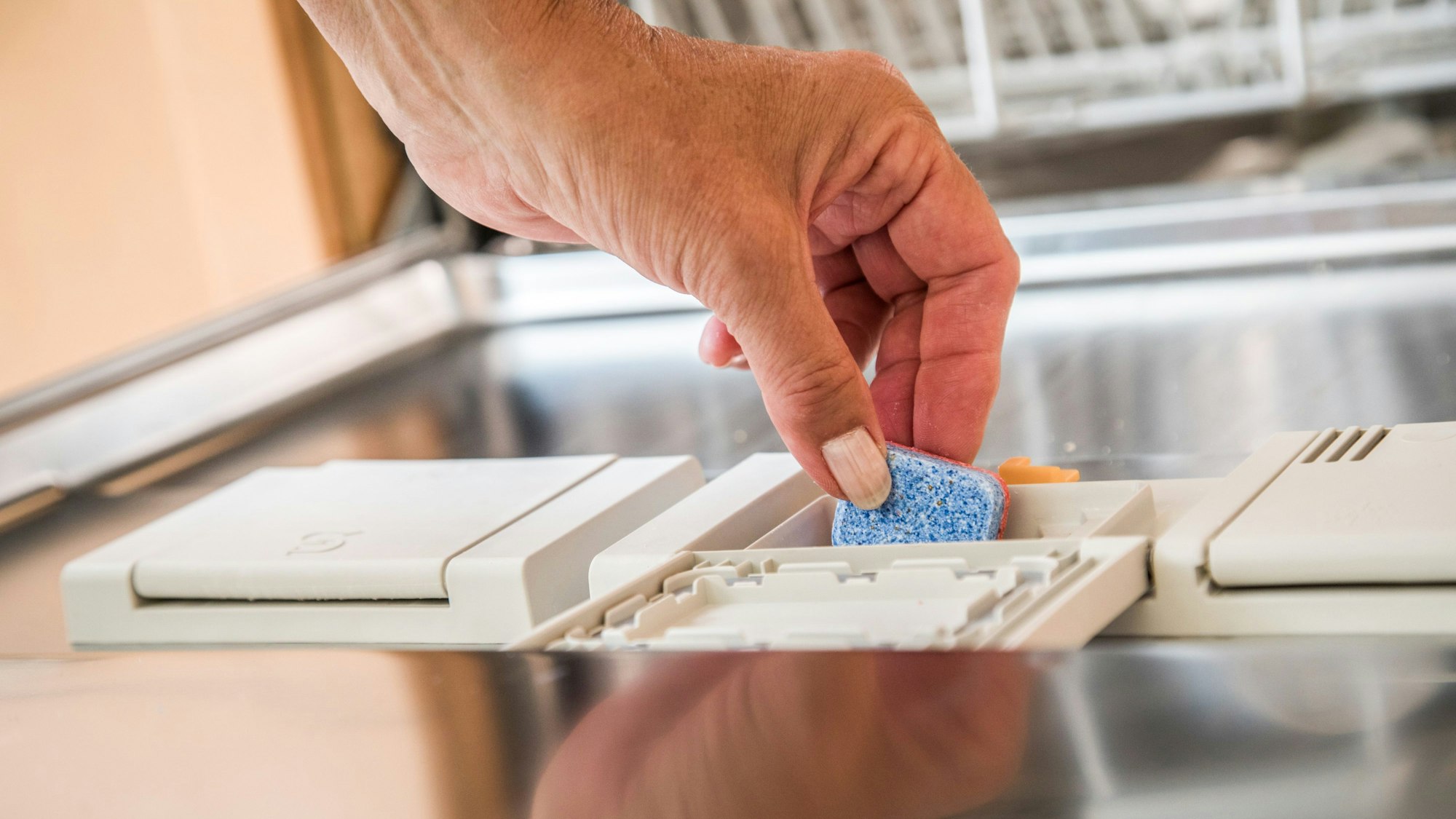Eine Person befüllt eine Geschirrsplämaschine mit einem Geschirrspültab.